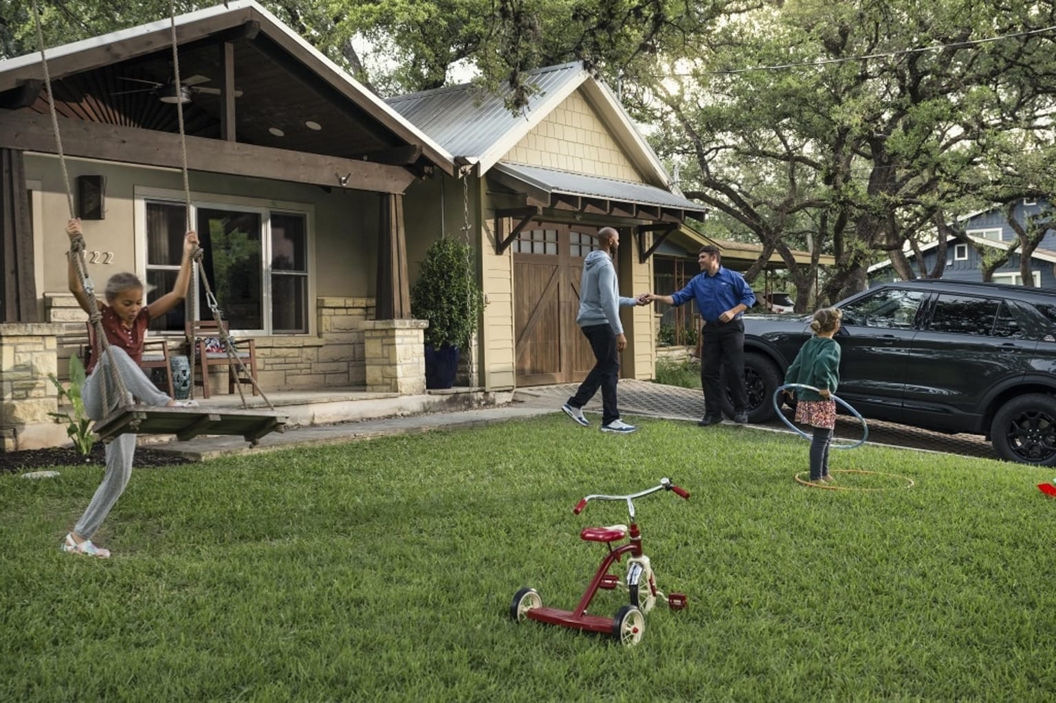 a group of people playing in a yard with a child on a swing set and a car parked in front of a house