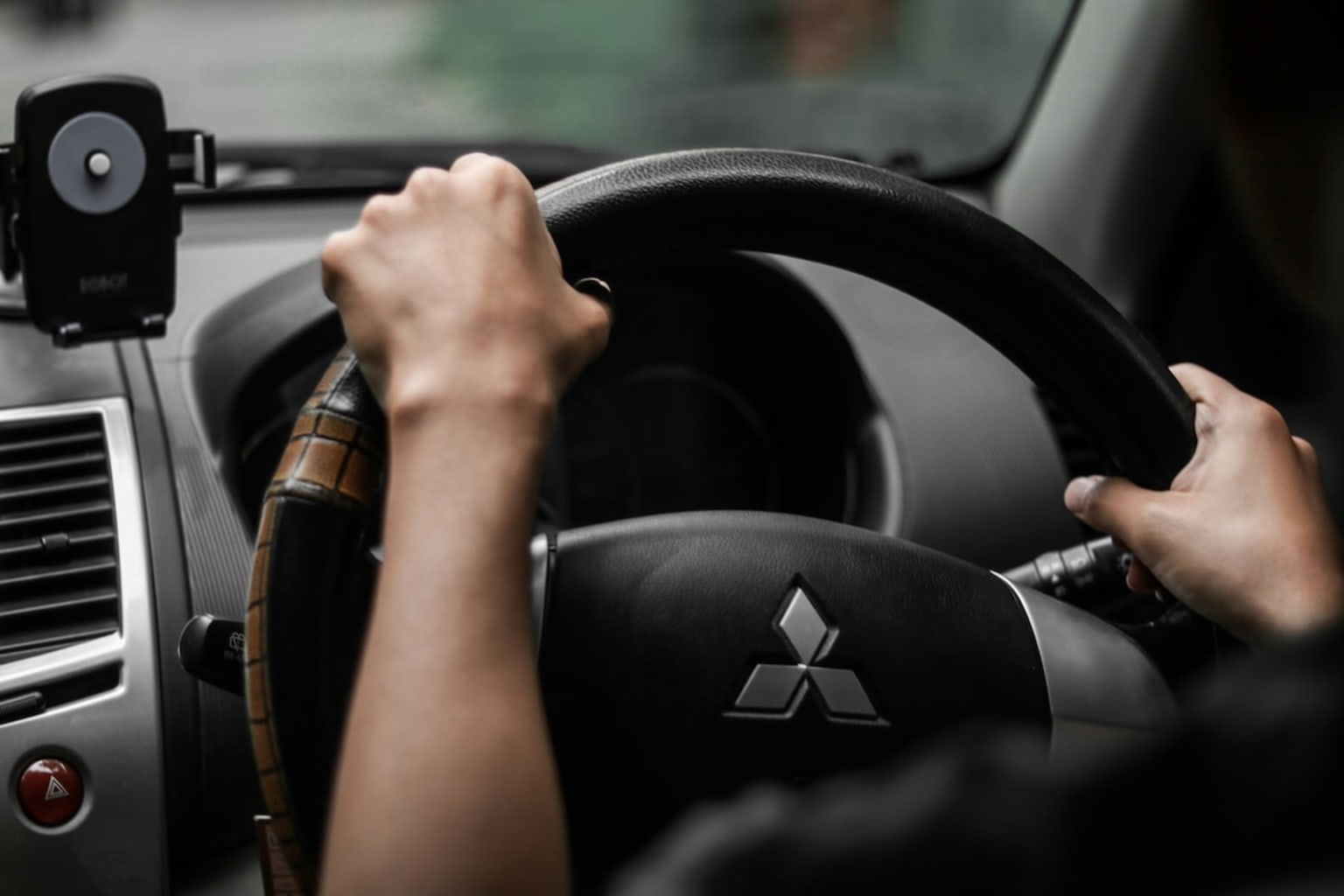 a person driving a car with a steering wheel and a hand on the steering wheel with a black dashboard