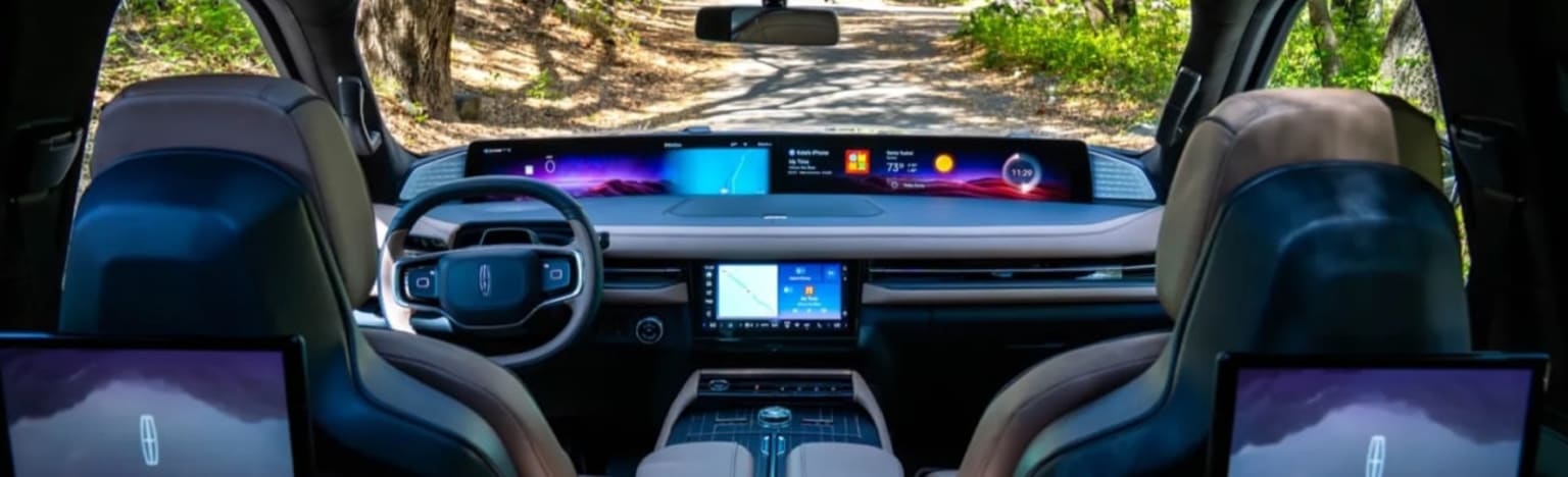 Interior of a modern car with multiple screens on a tree-lined road.
