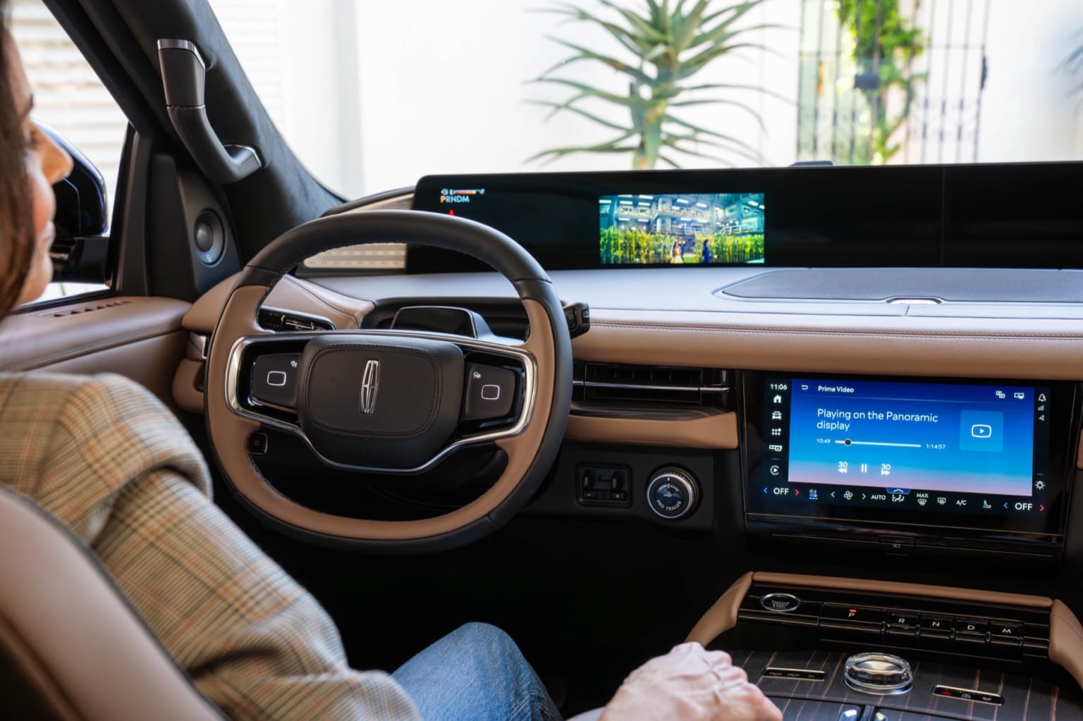 Interior of a modern car with steering wheel, dashboard, and large touchscreen display displaying a navigation map, surrounded by a lush green outdoor environment visible through the windows.