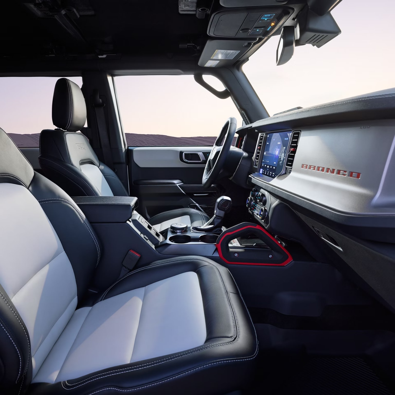 Interior of a modern vehicle with a sleek dashboard, comfortable leather seats, and a large central display screen. Outdoor setting with a sunset or sunrise visible through the windshield.
