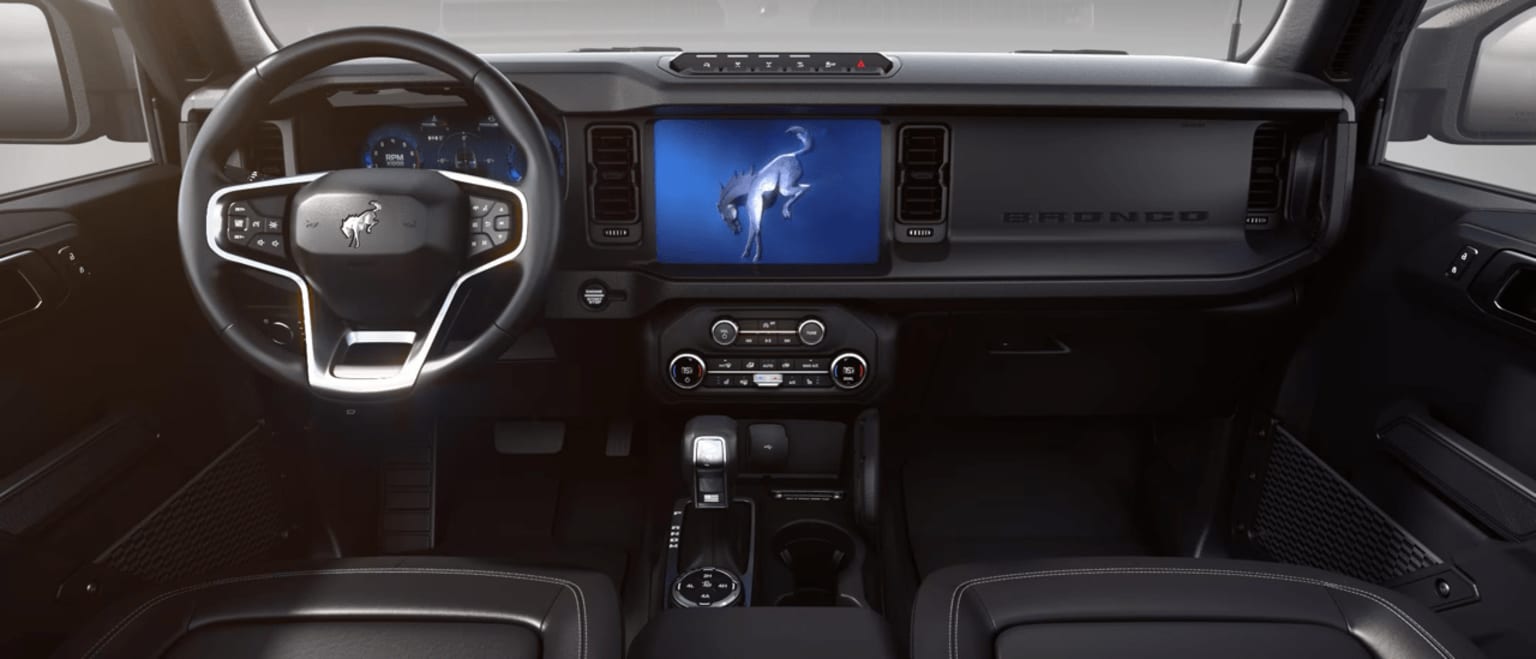 Interior of a vehicle with a large display screen in the center console showing an image of a whale or dolphin jumping out of the water.