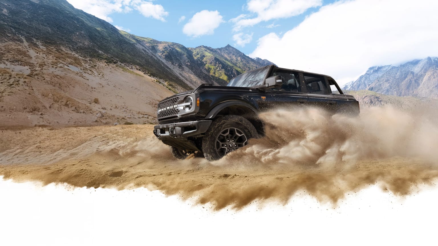 Off-road vehicle driving through dusty, mountainous terrain with rocky peaks and cloudy sky in the background