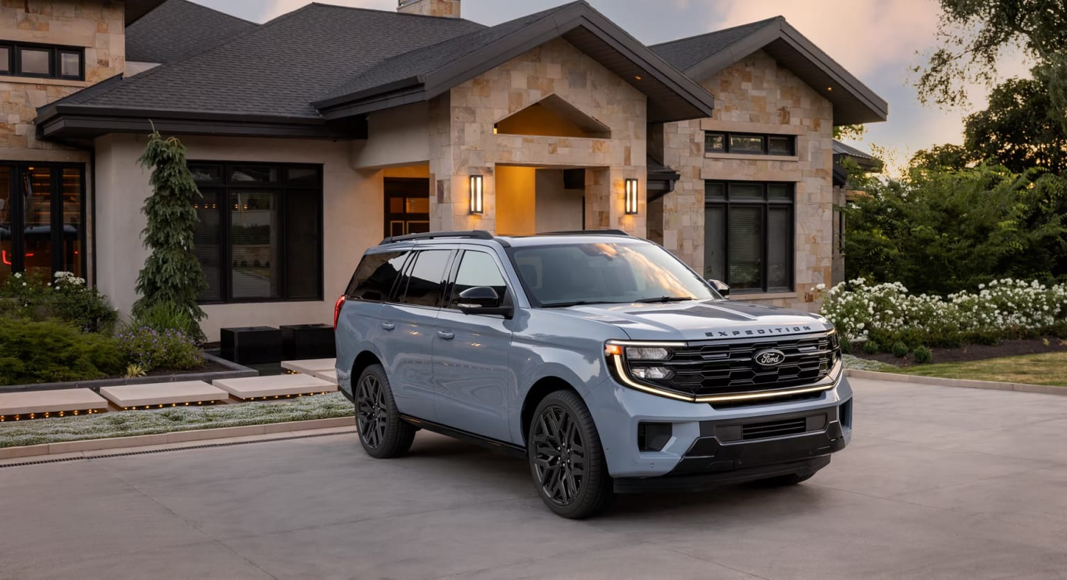 A large, modern-looking house with a distinctive architectural style, featuring a prominent roofline and large windows, stands in the background, while a silver SUV is parked in the foreground.