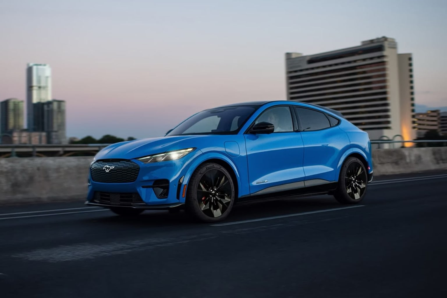 Electric SUV parked on city street with modern high-rise building in background at sunset.