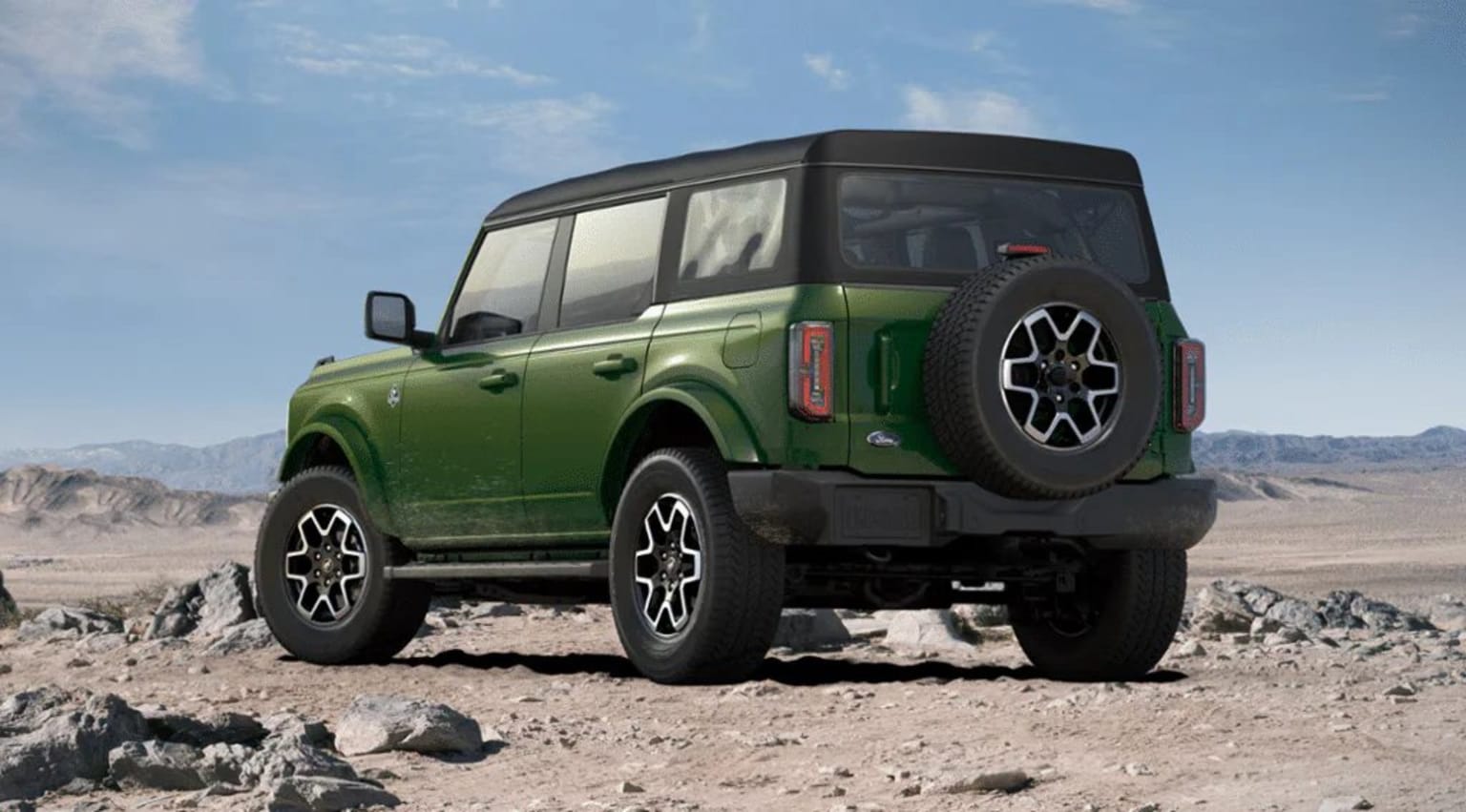 Off-road vehicle with large tires parked in desert landscape with rocky formations in background.