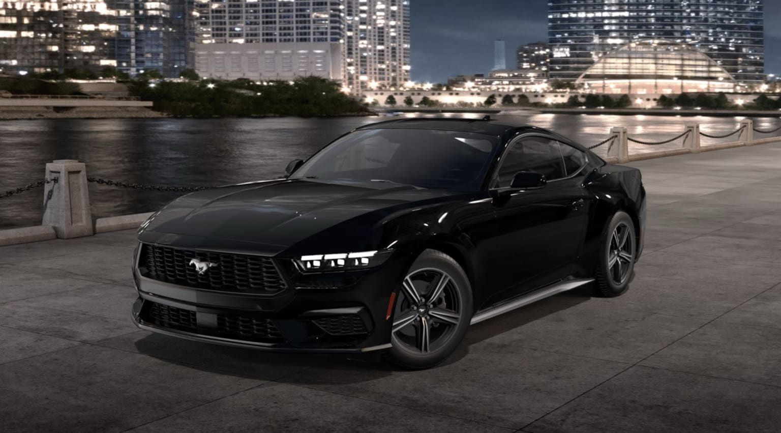 Black sports car parked on a riverfront promenade with high-rise buildings in the background.