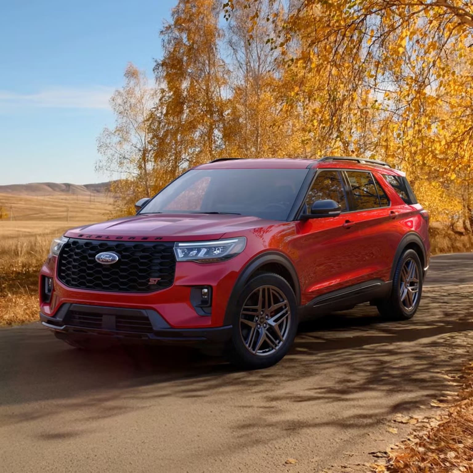 Red SUV parked on a dirt road with autumn trees in the background
