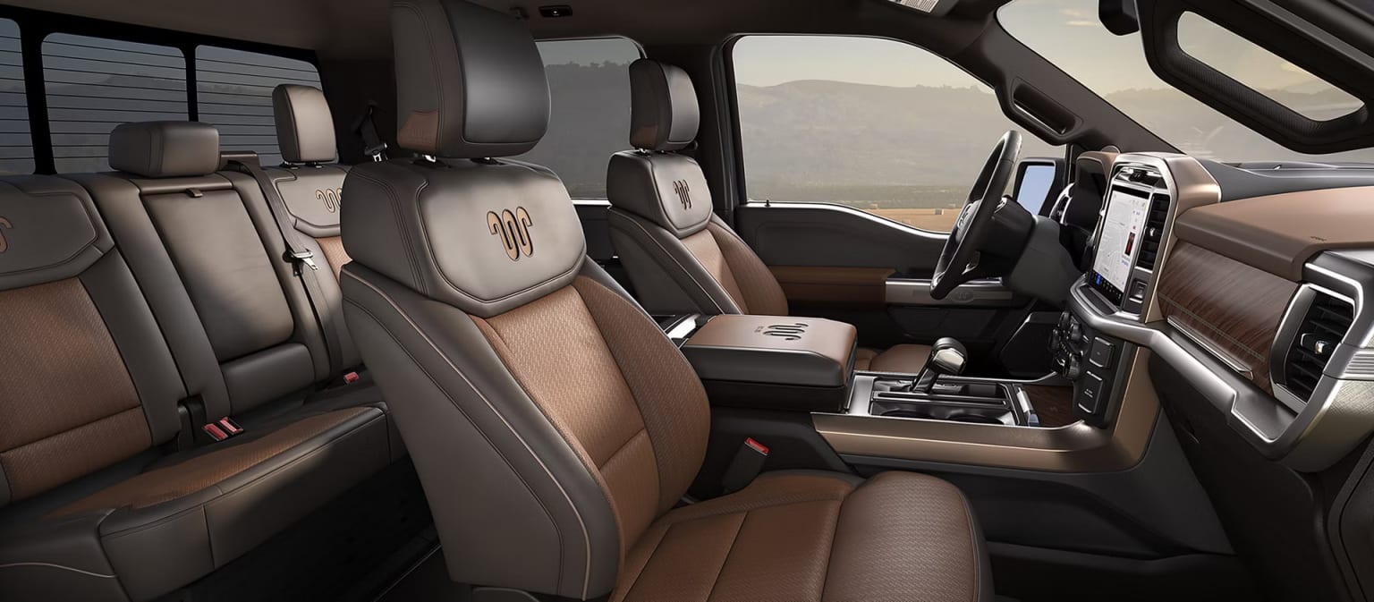 Brown and black leather seats with embroidered logos in the foreground of a car interior, with a hazy, desert-like landscape visible through the windows in the background.