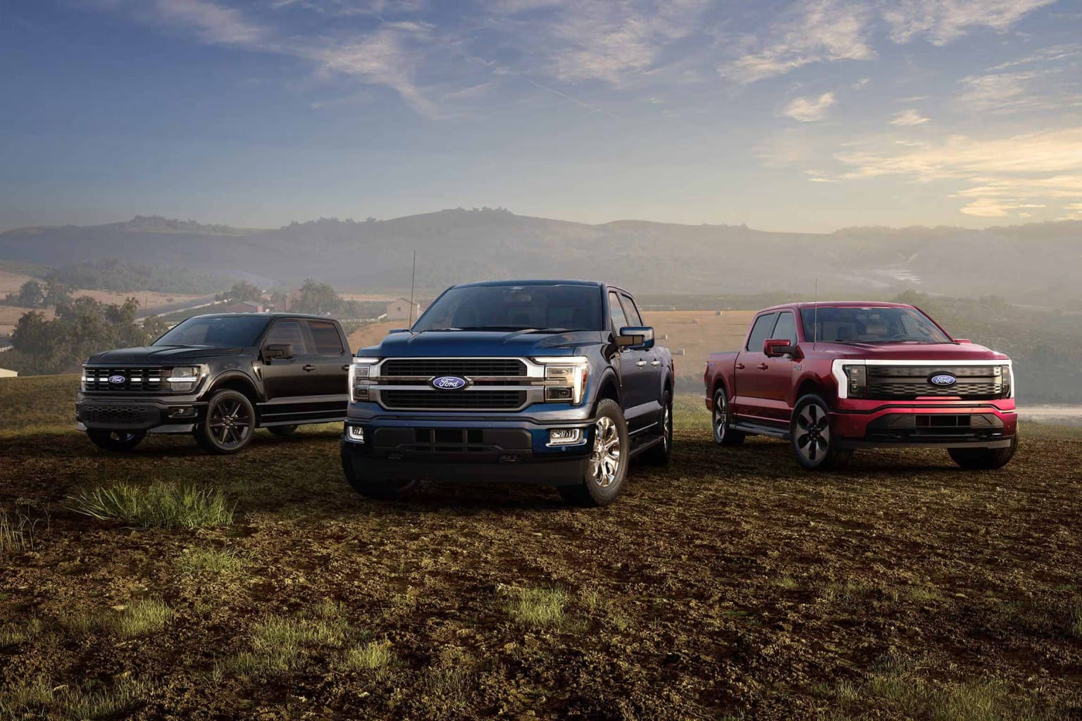 Several pickup trucks parked on a grassy field with mountains in the background.