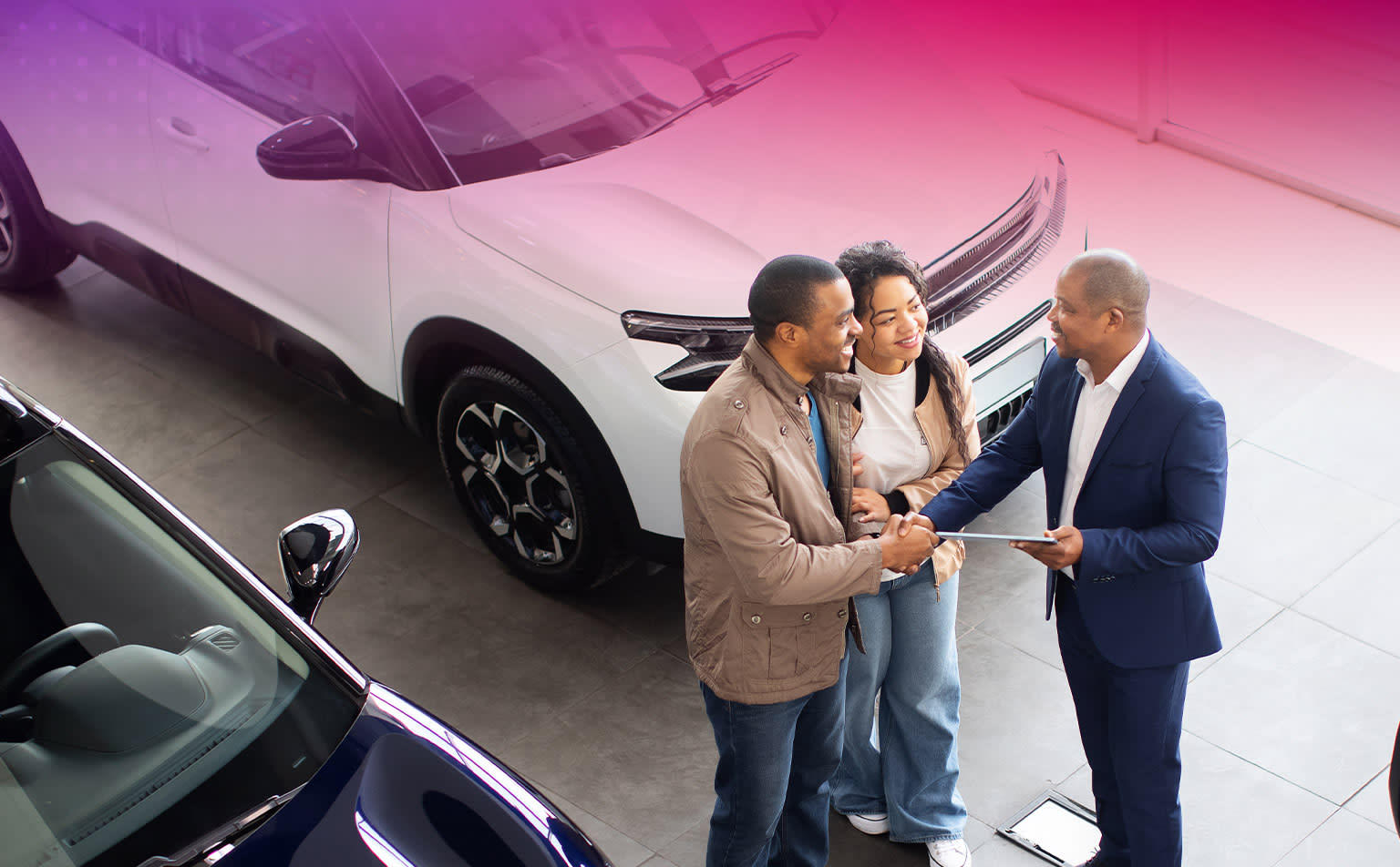 Three individuals, two men and one woman, standing in a car showroom or dealership. The individuals are engaged in conversation, with one man gesturing while the other two listen intently. Background features a large, sleek-looking car on display, with its distinctive design and features visible.
