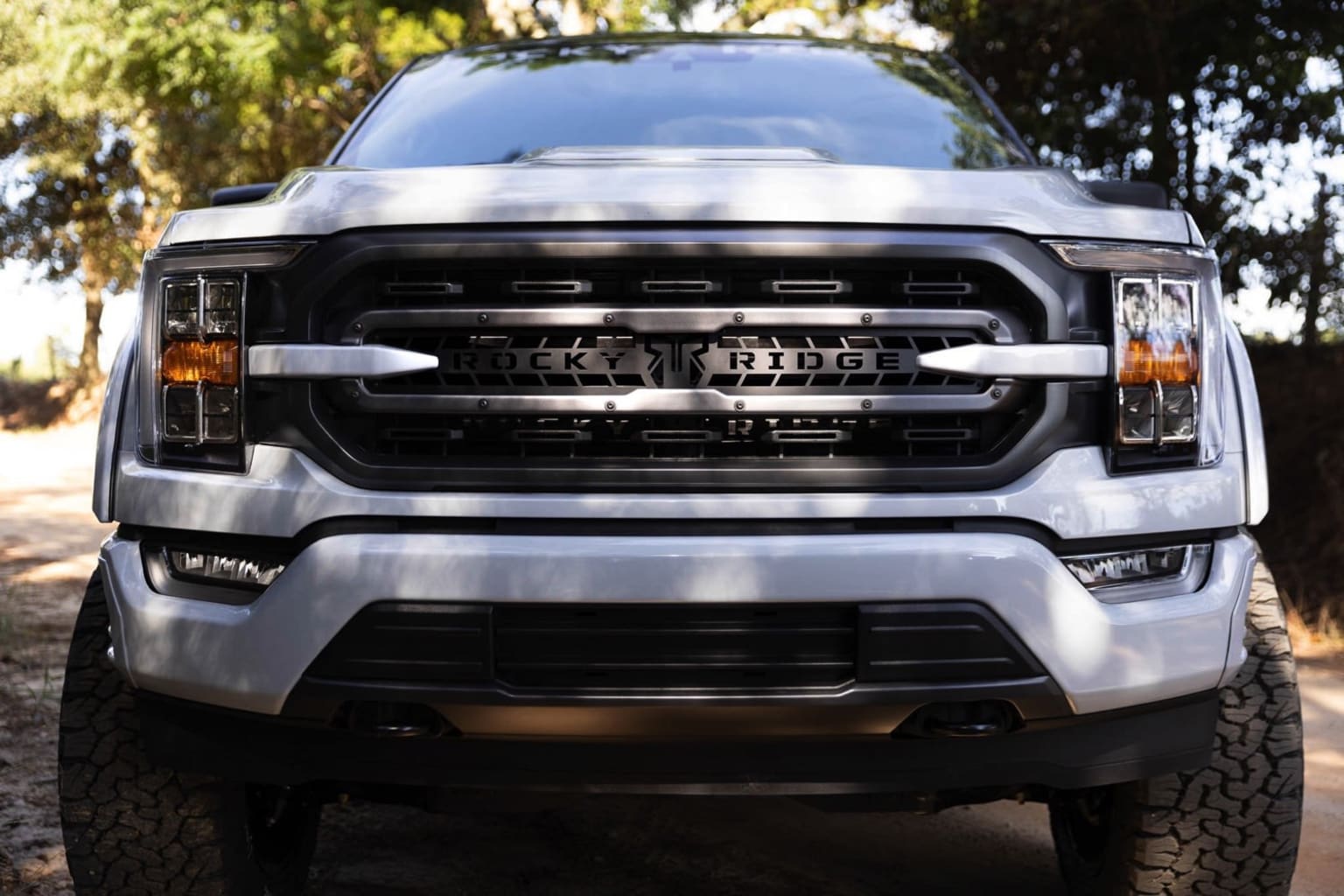 An off-road-ready pickup truck stands prominently in the foreground, surrounded by a lush, verdant landscape in the background.