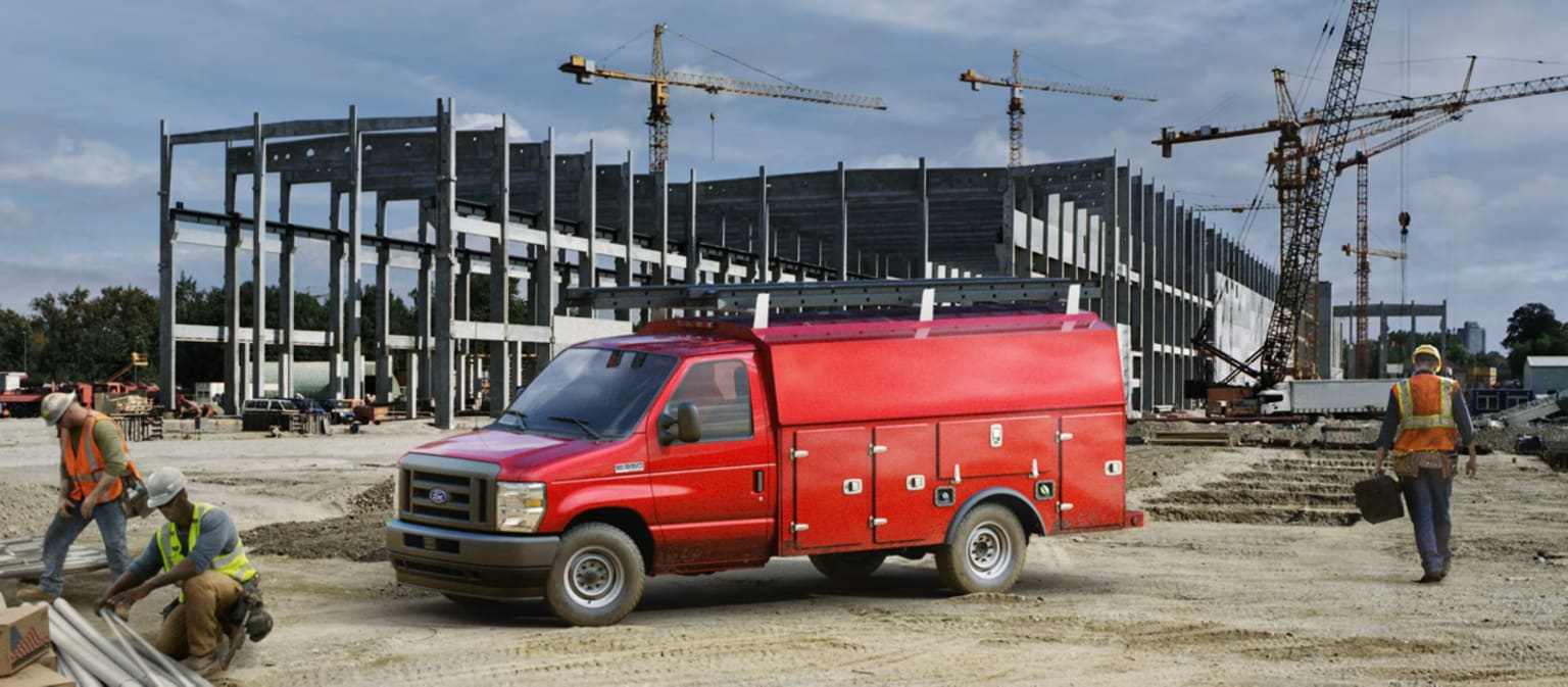 A red utility van parked in the foreground of a construction site, with several cranes and partially built structures visible in the background.