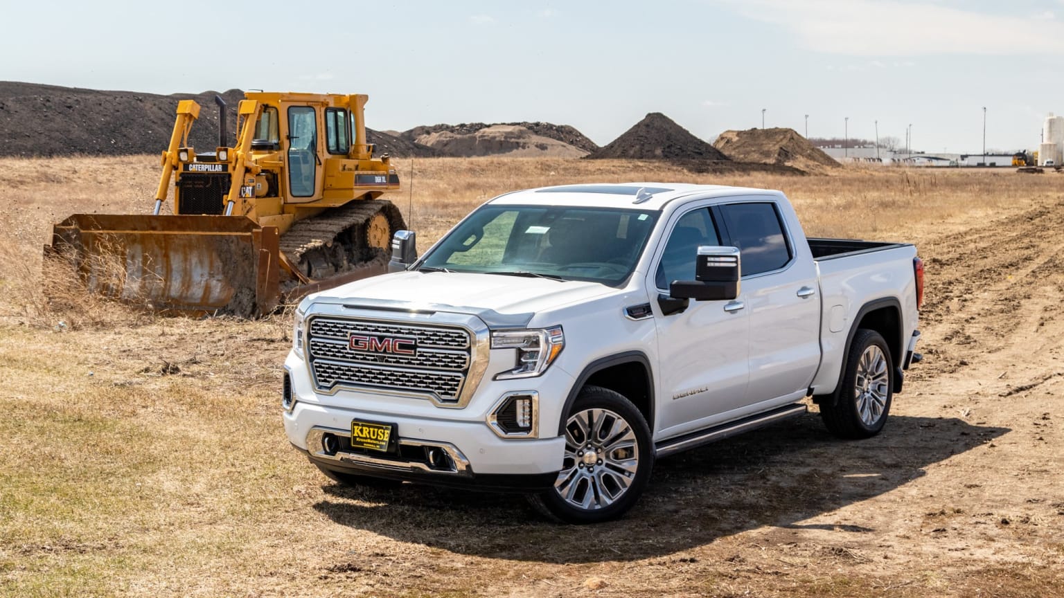 a white truck parked on a dirt road next to a bulldozer in the middle of a field