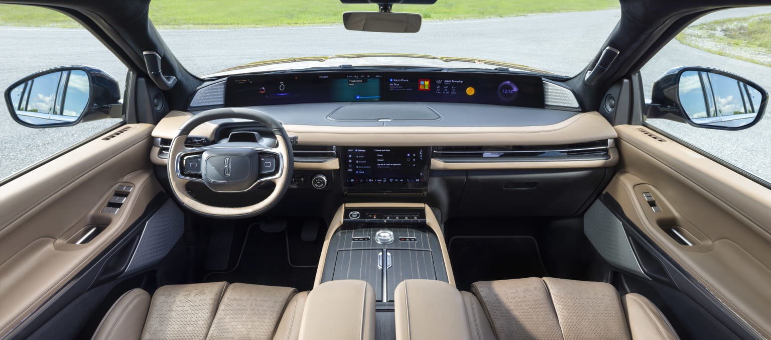 The image depicts the interior of a modern vehicle with a sleek dashboard, a large central display, and a steering wheel. The background outside the vehicle resembles a grassy field or lawn.