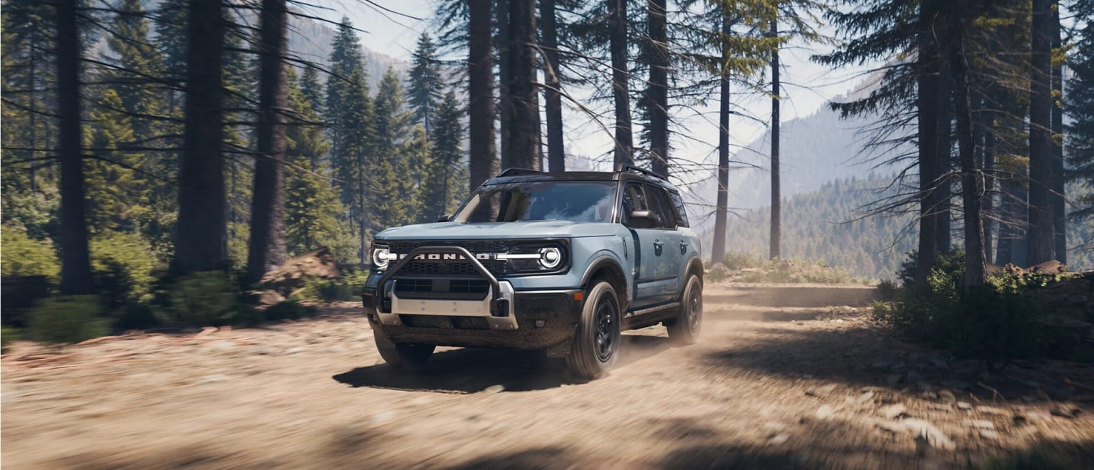 Off-road vehicle exploring a dirt path in a dense evergreen forest with misty atmosphere.
