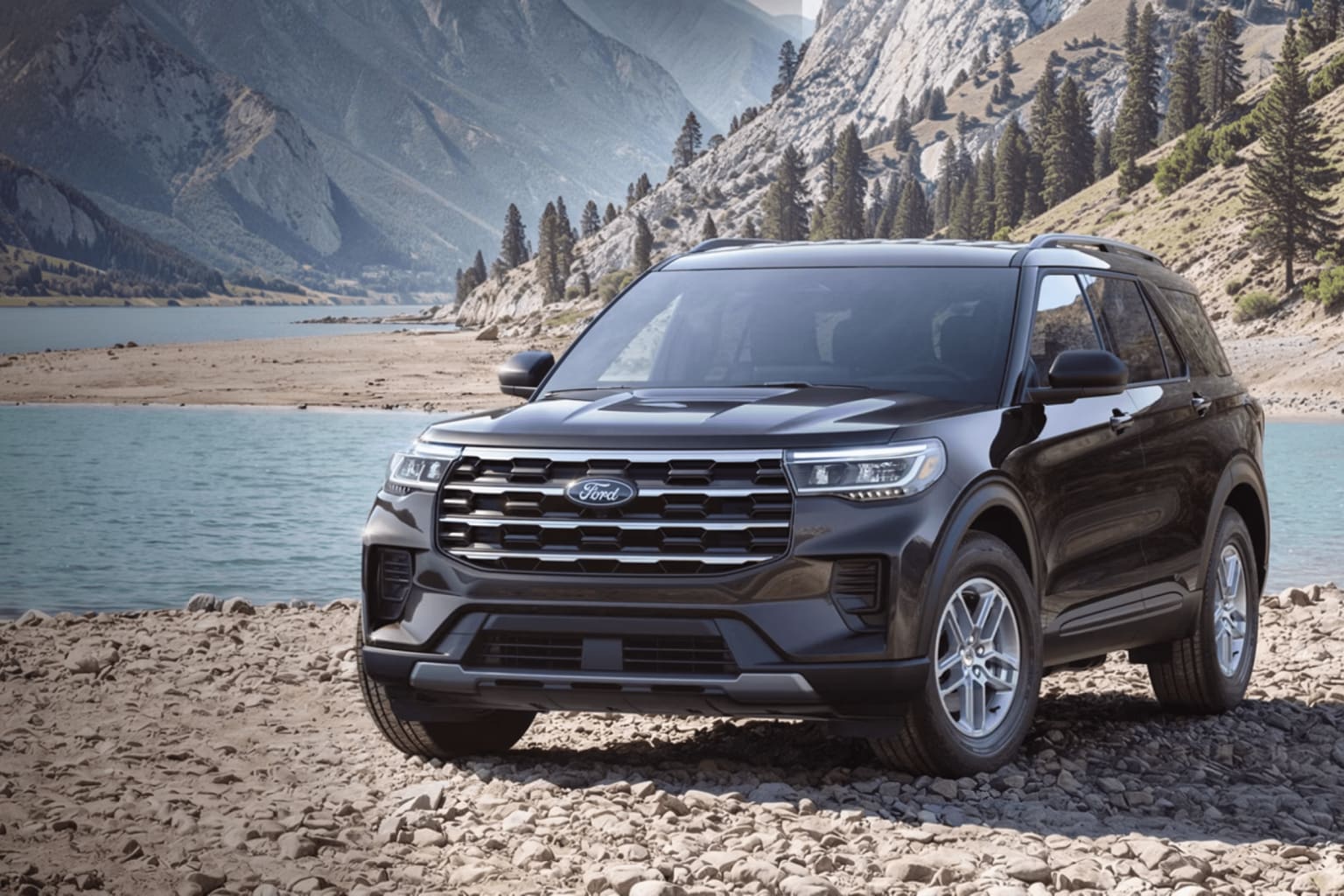 A black SUV is parked on a rocky shore with a lake and mountains in the background.