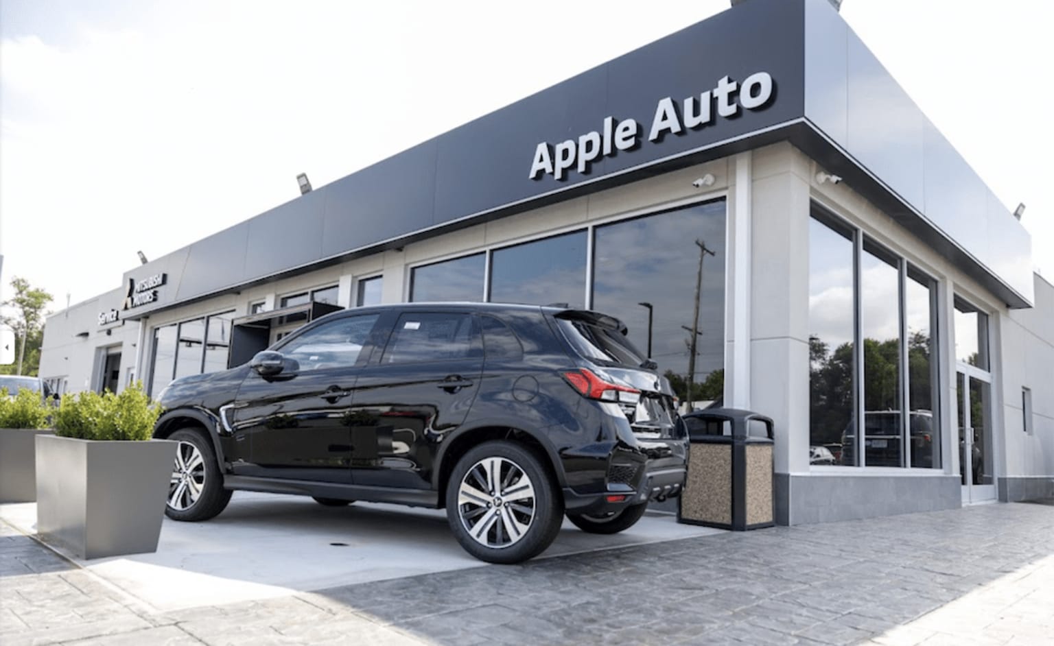 a black car is parked outside of an apple auto showroom in front of a building with a sign that says apple auto