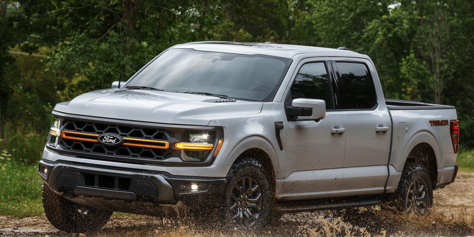 An off-road pickup truck with a distinctive grille and large tires in a lush, green forest setting.