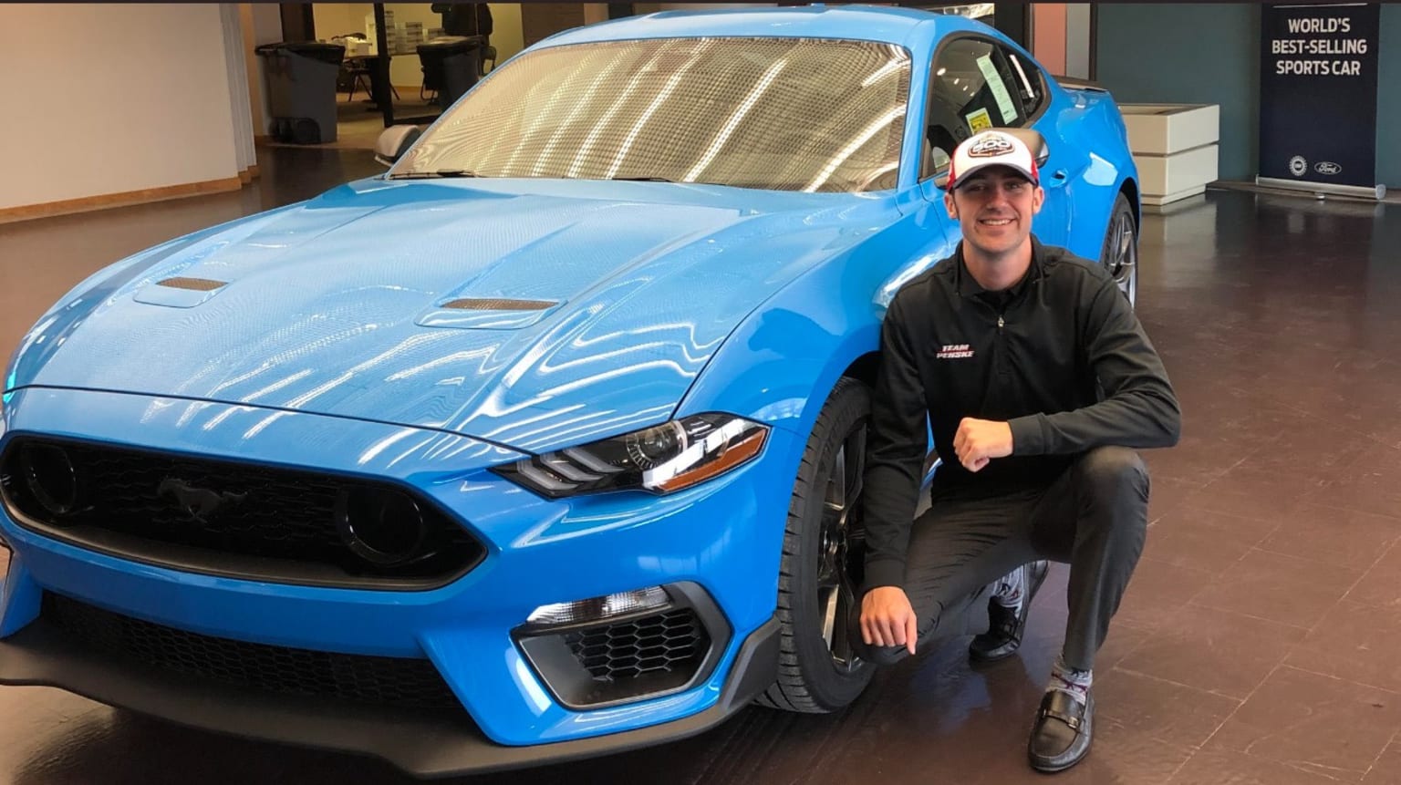 a man kneeling down next to a blue car in a showroom with a blue mustang on the front of the car