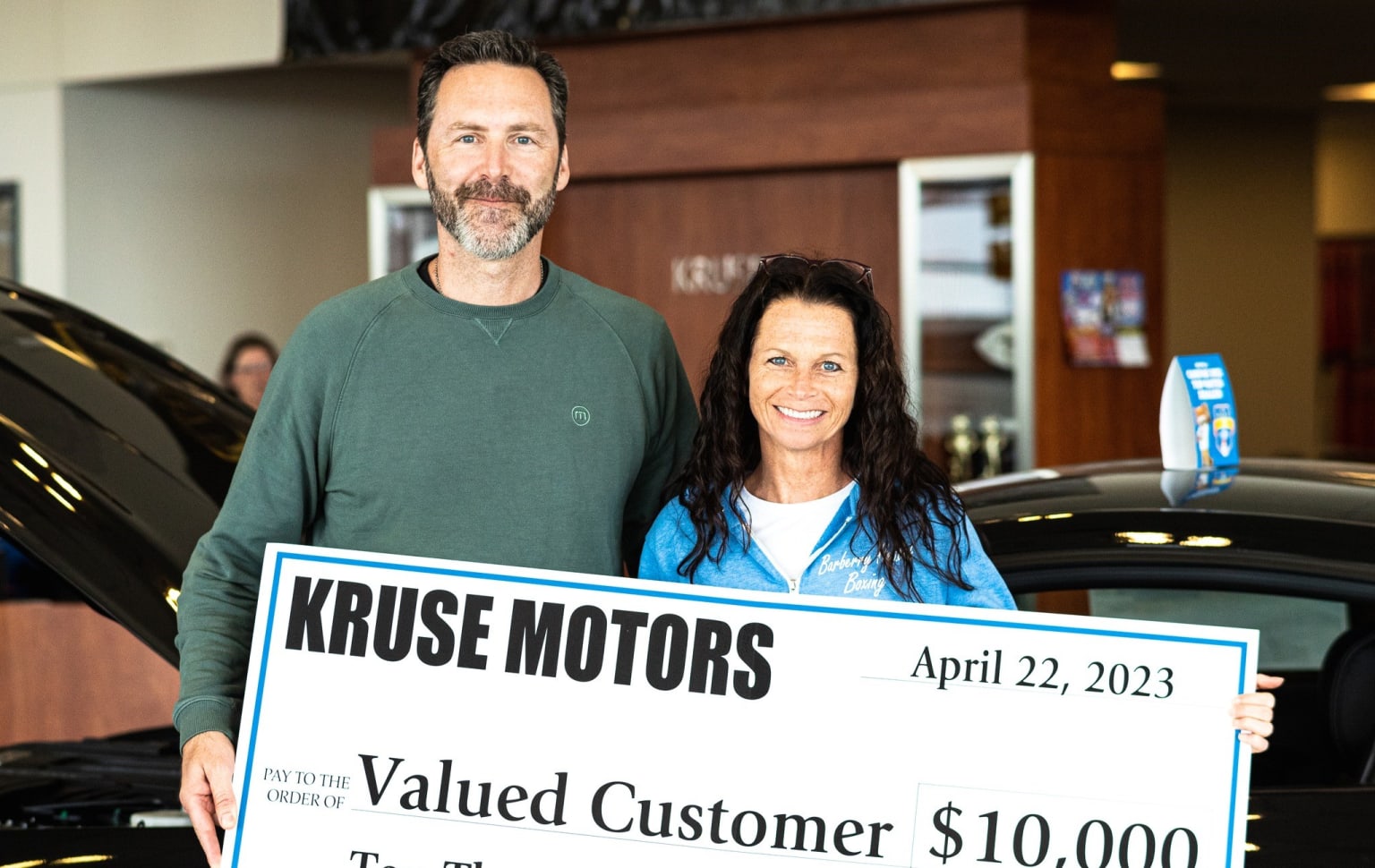a man and a woman holding a large check for $ 10, 000 in front of a black car