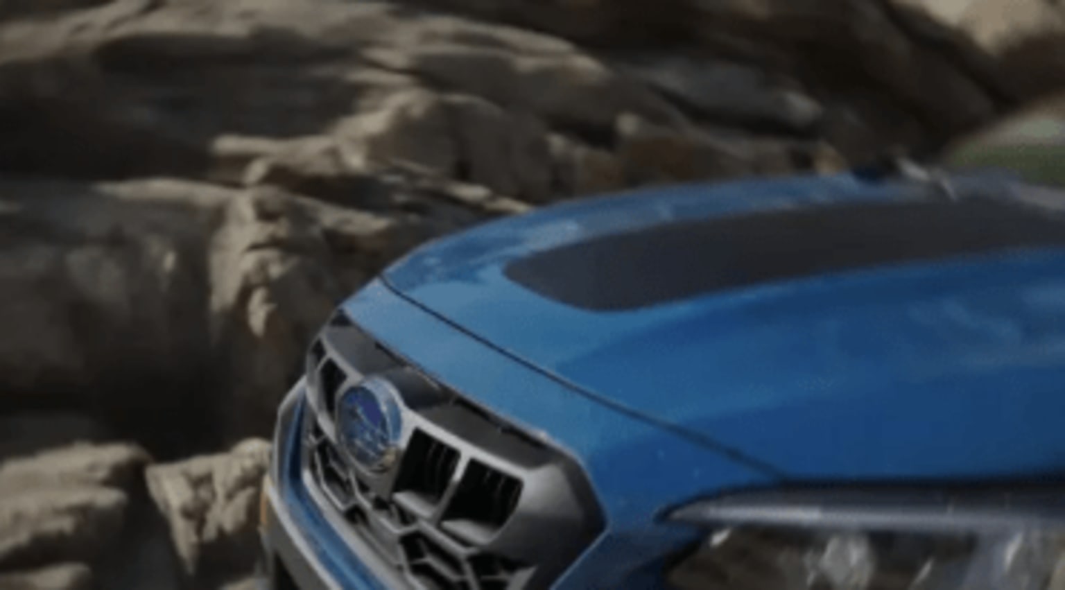A blue car parked in front of a rocky, snow-covered landscape.