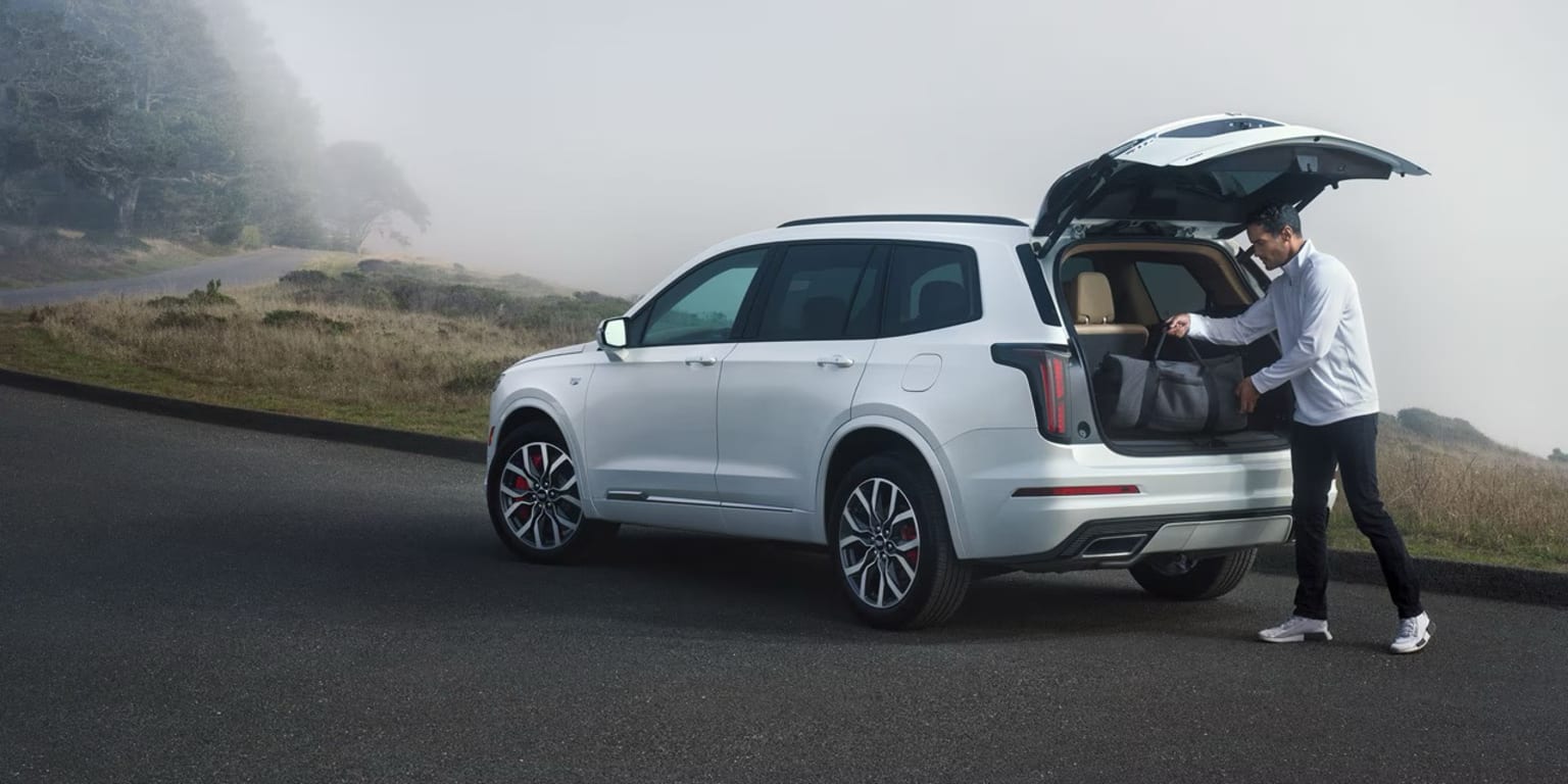 White SUV parked on a road with misty hills and trees in the background.