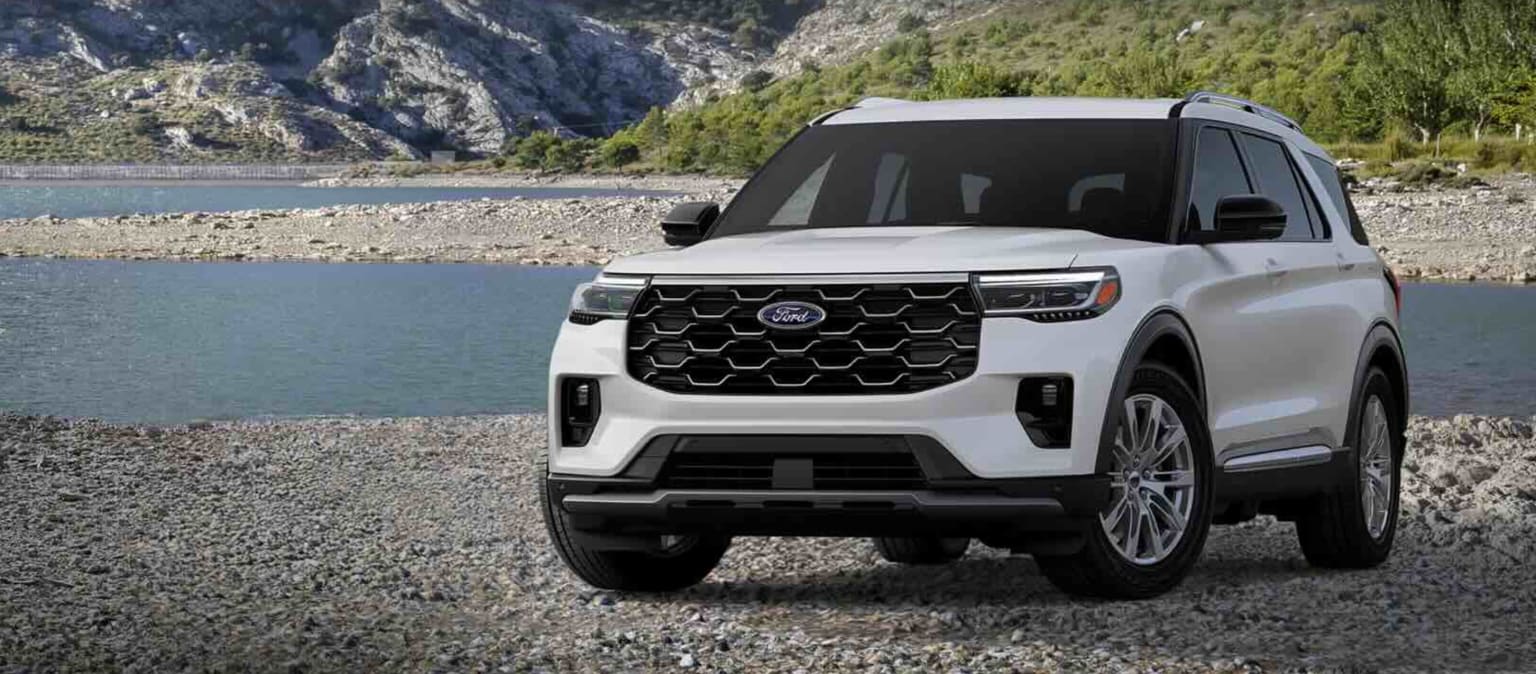 SUV parked on rocky shore with river and mountains in background.