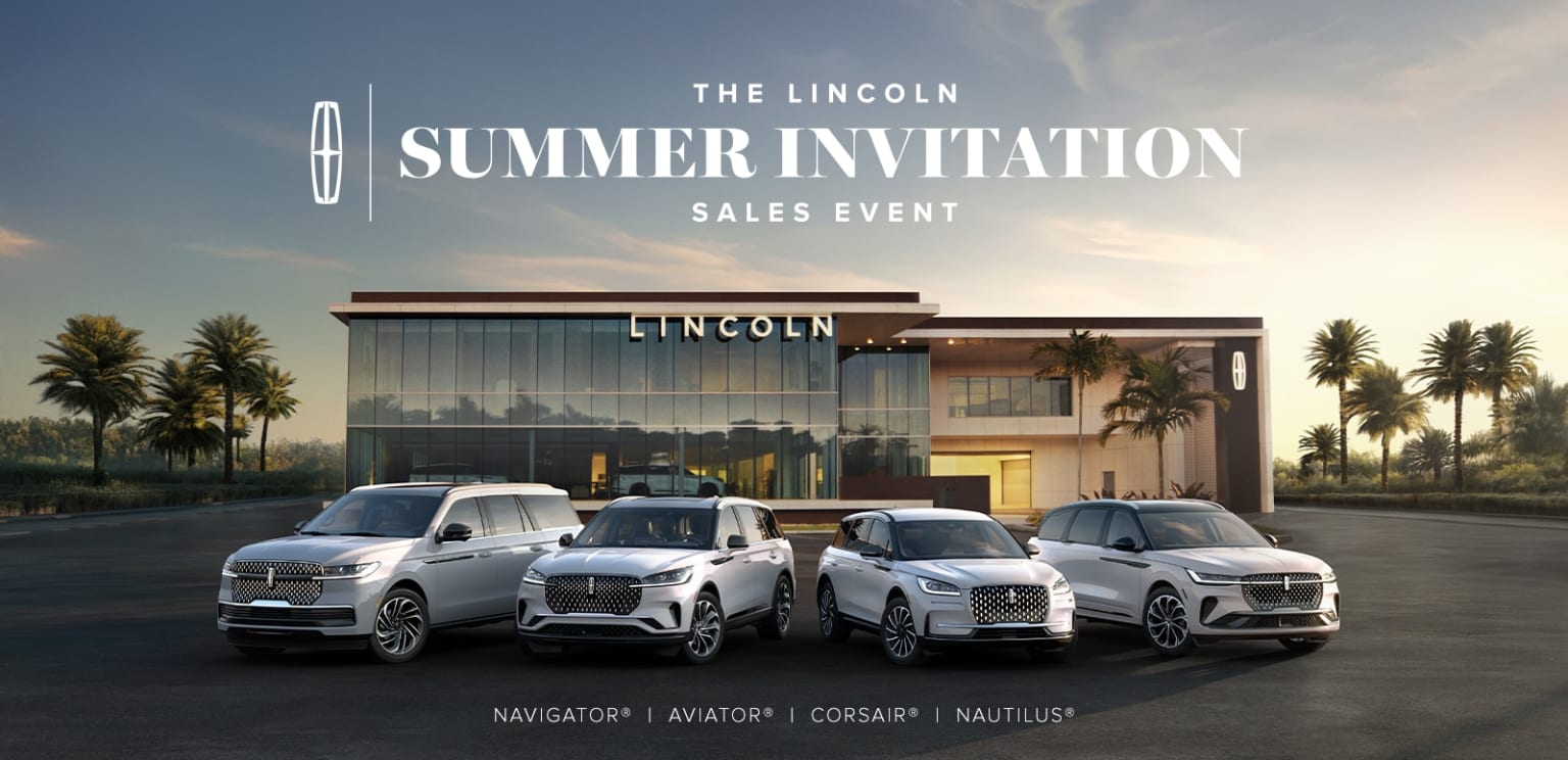 A modern dealership building surrounded by palm trees, with several vehicles prominently displayed in the foreground.