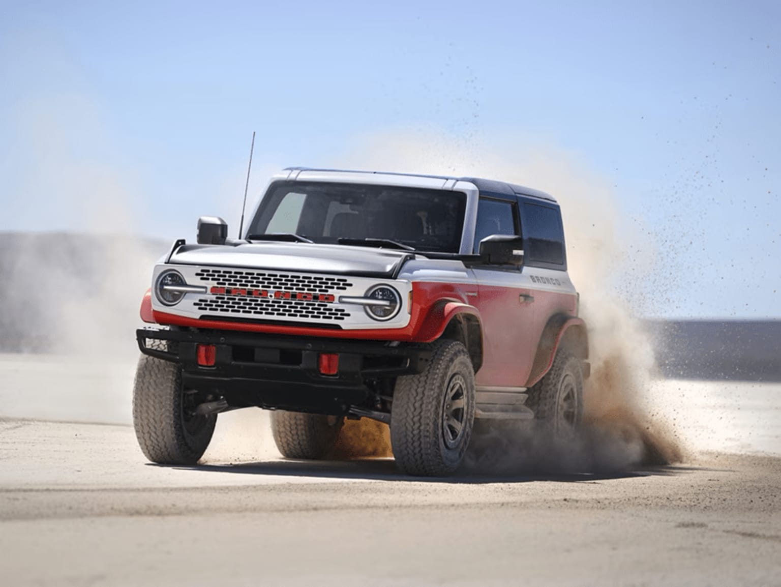 Off-road vehicle kicking up dust in desert landscape under clear blue sky.