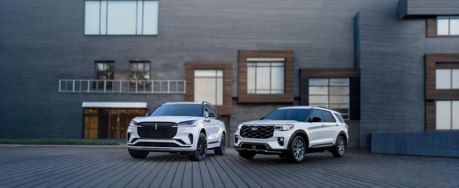 Luxury SUVs parked on a wooden deck in front of a modern building with large windows.