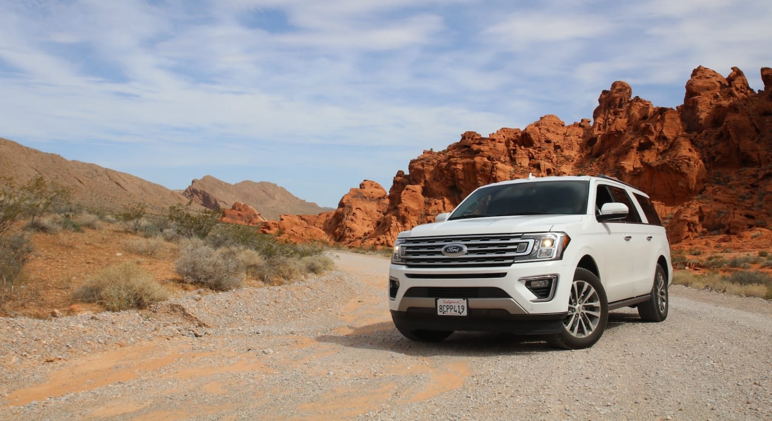 a white suv is parked on a gravel road in front of a rocky outcropping in the desert