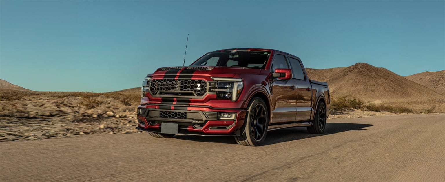 A red and black pickup truck stands in a desert landscape with a rocky hill in the background.