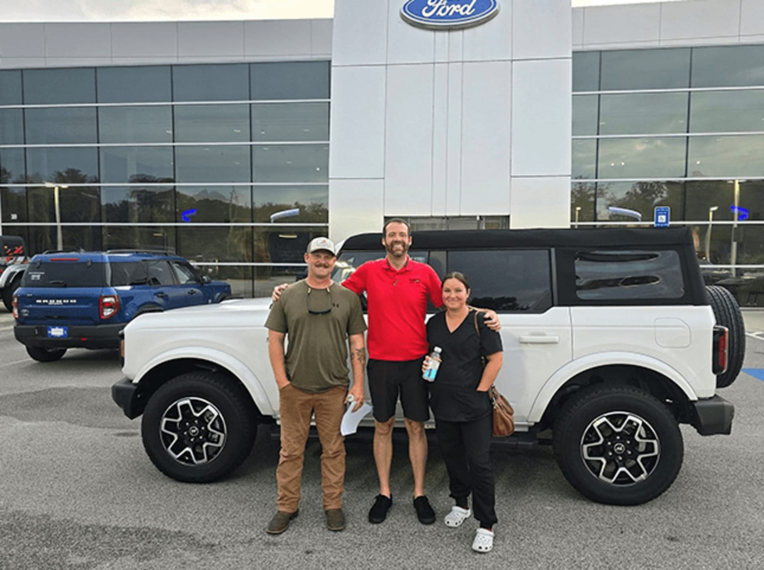 Three people standing in front of a large white pickup truck at a car dealership.
