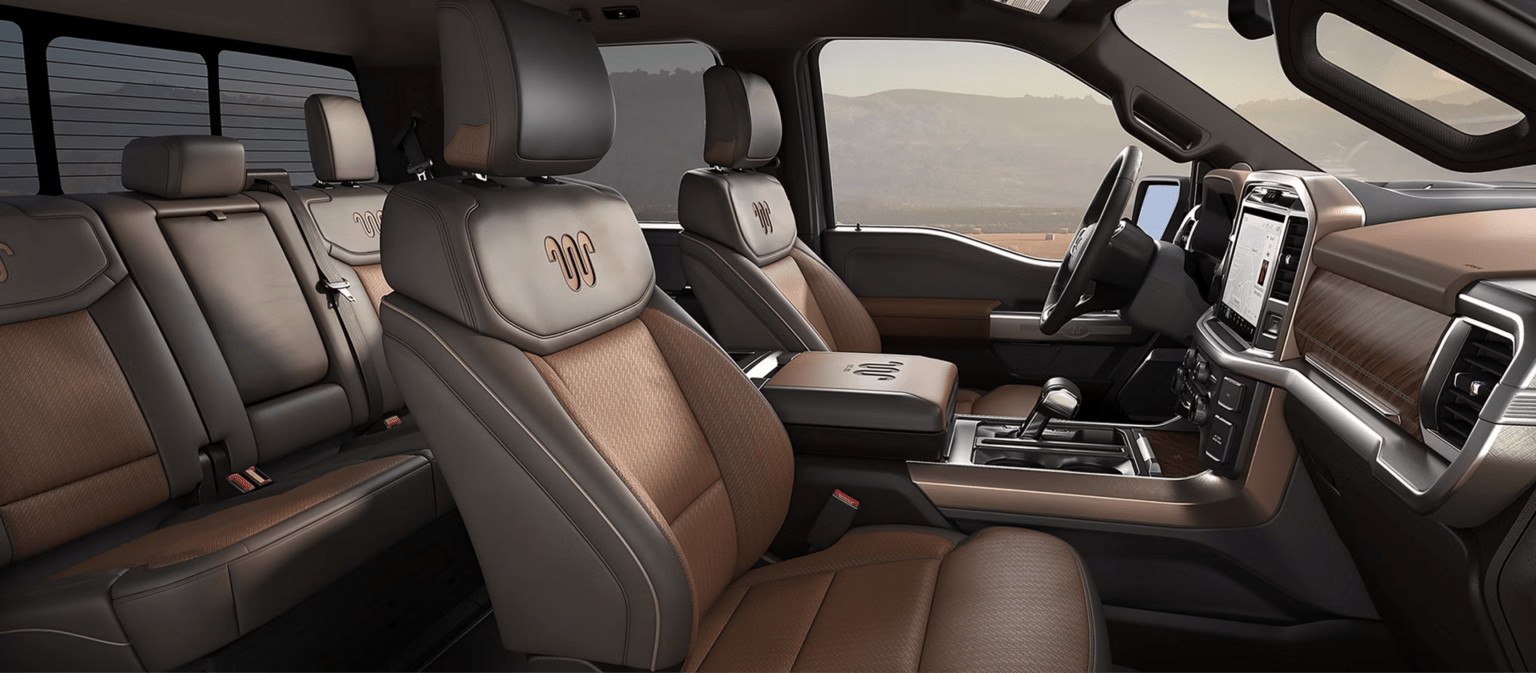 Brown and black leather seats with embroidered logos in the foreground, with a hazy desert-like landscape visible through the windows in the background.