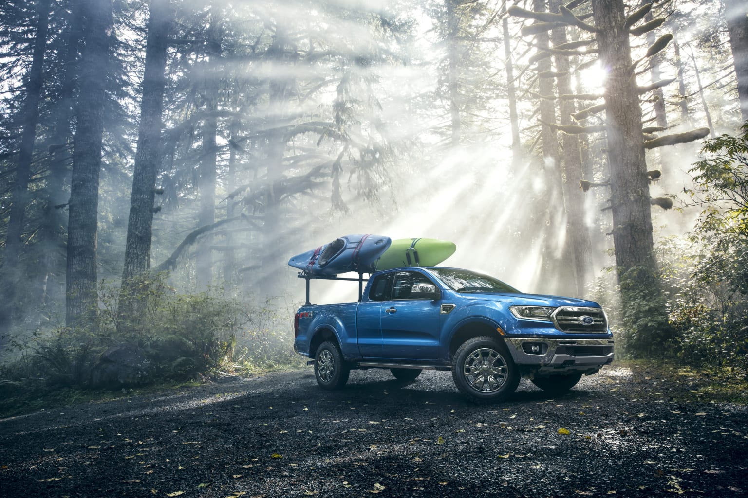 a blue pick up truck with a kayak on top of it's roof parked in the middle of a forest