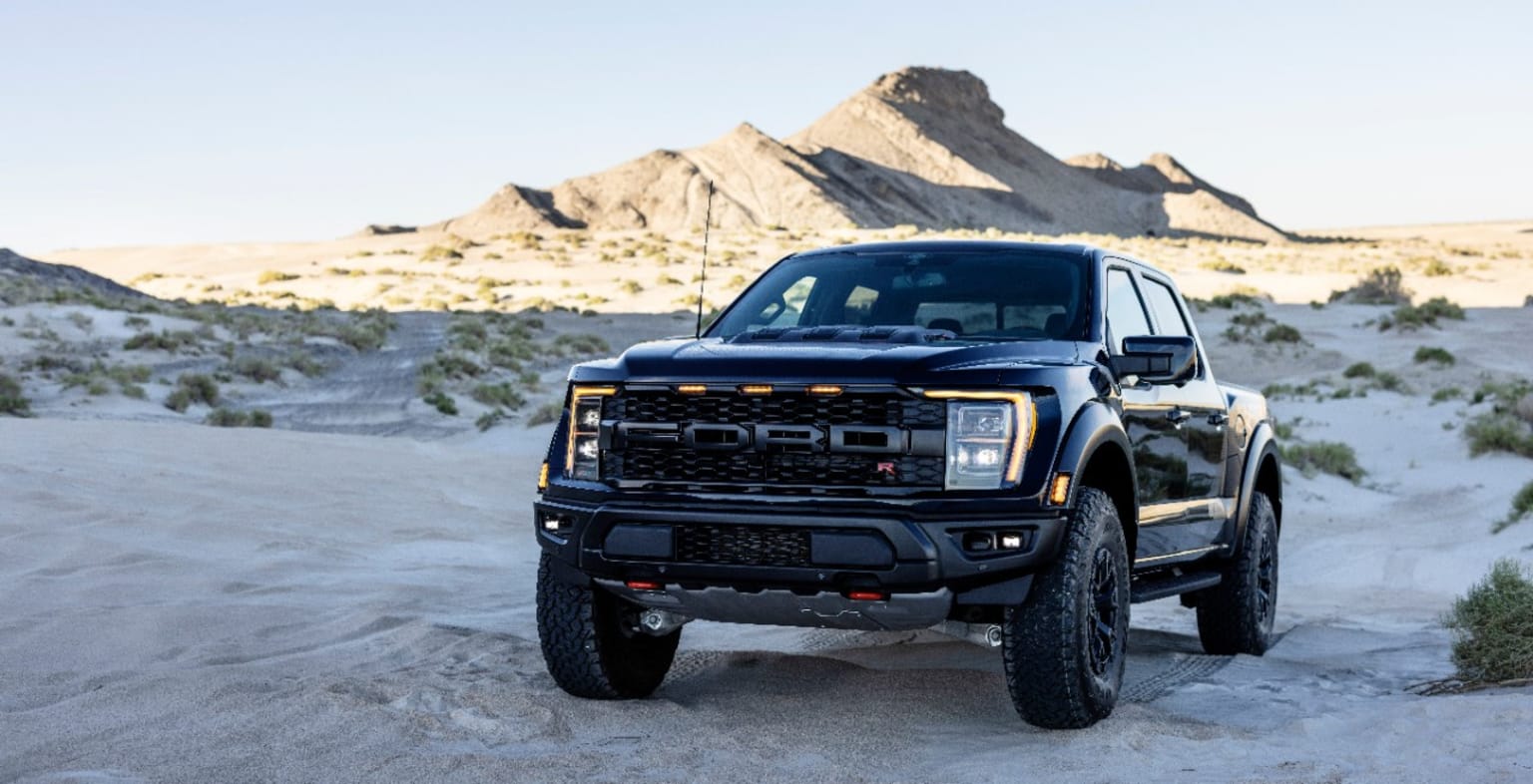 a black truck parked in the middle of a sandy area with mountains in the background and a blue sky in the background