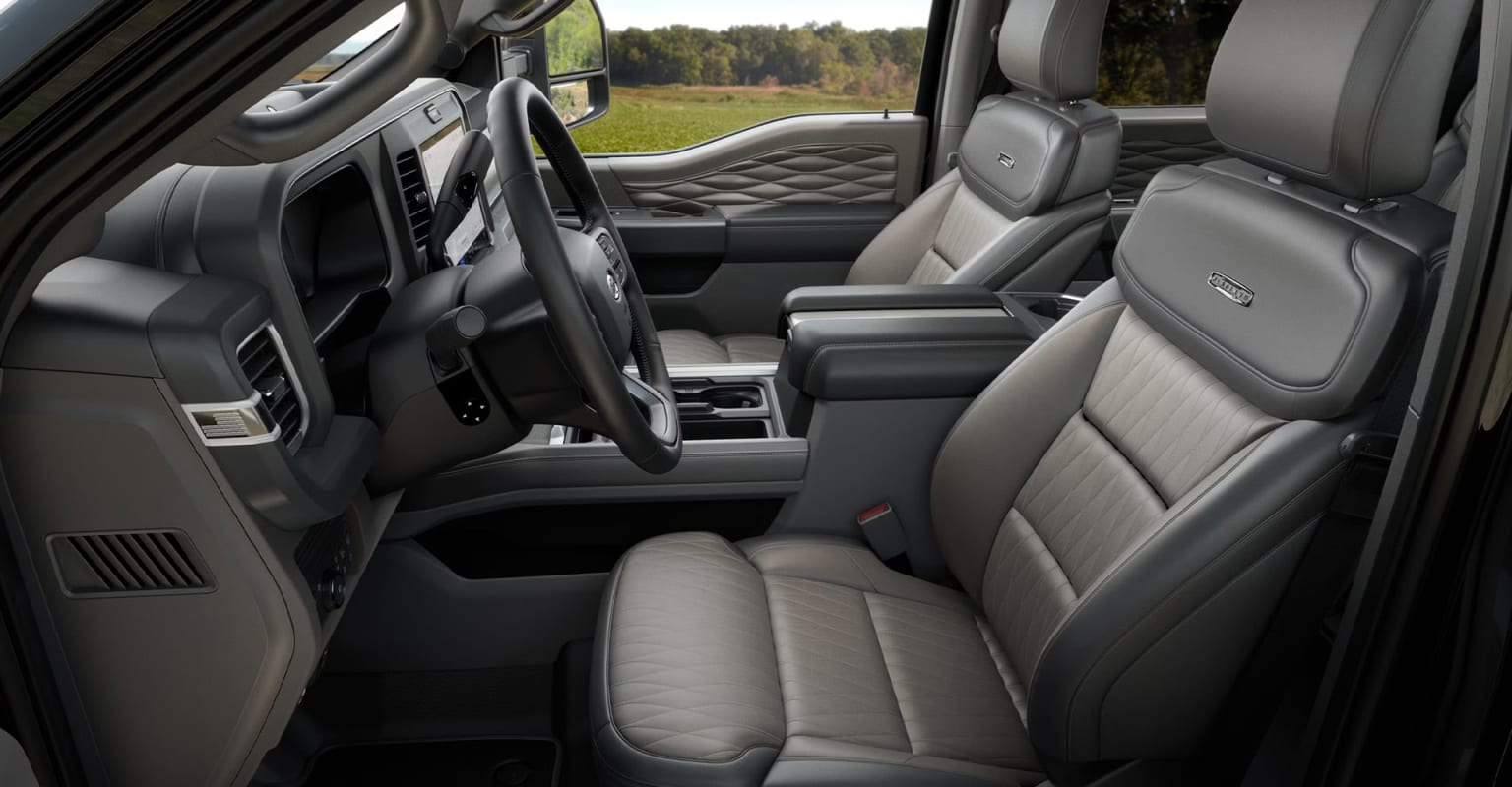 Interior of a vehicle with spacious and well-designed cabin, featuring comfortable leather seats, central console, and various controls and displays. Background outside the vehicle is a rural landscape with trees and open fields.