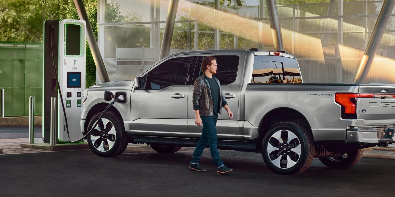 A woman standing next to a silver pickup truck.