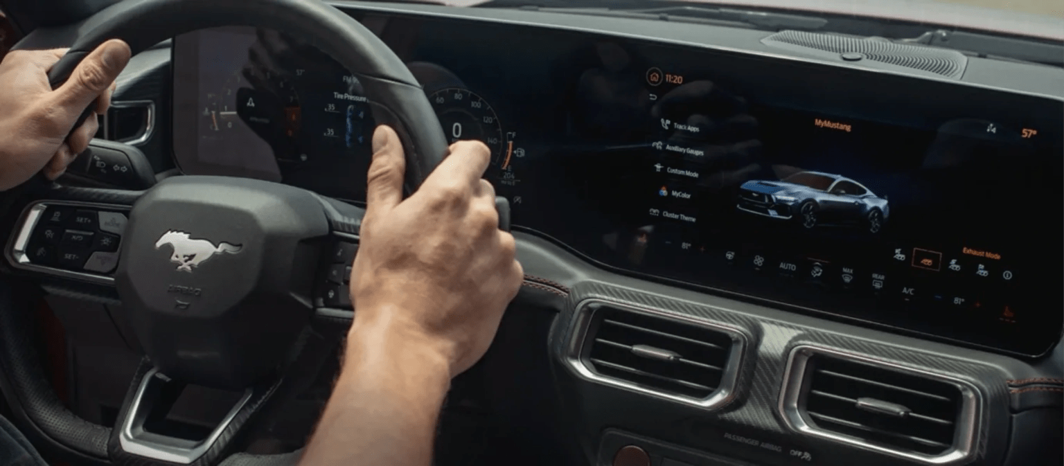 Person holding the steering wheel of a modern car with a digital dashboard showing a sports car.