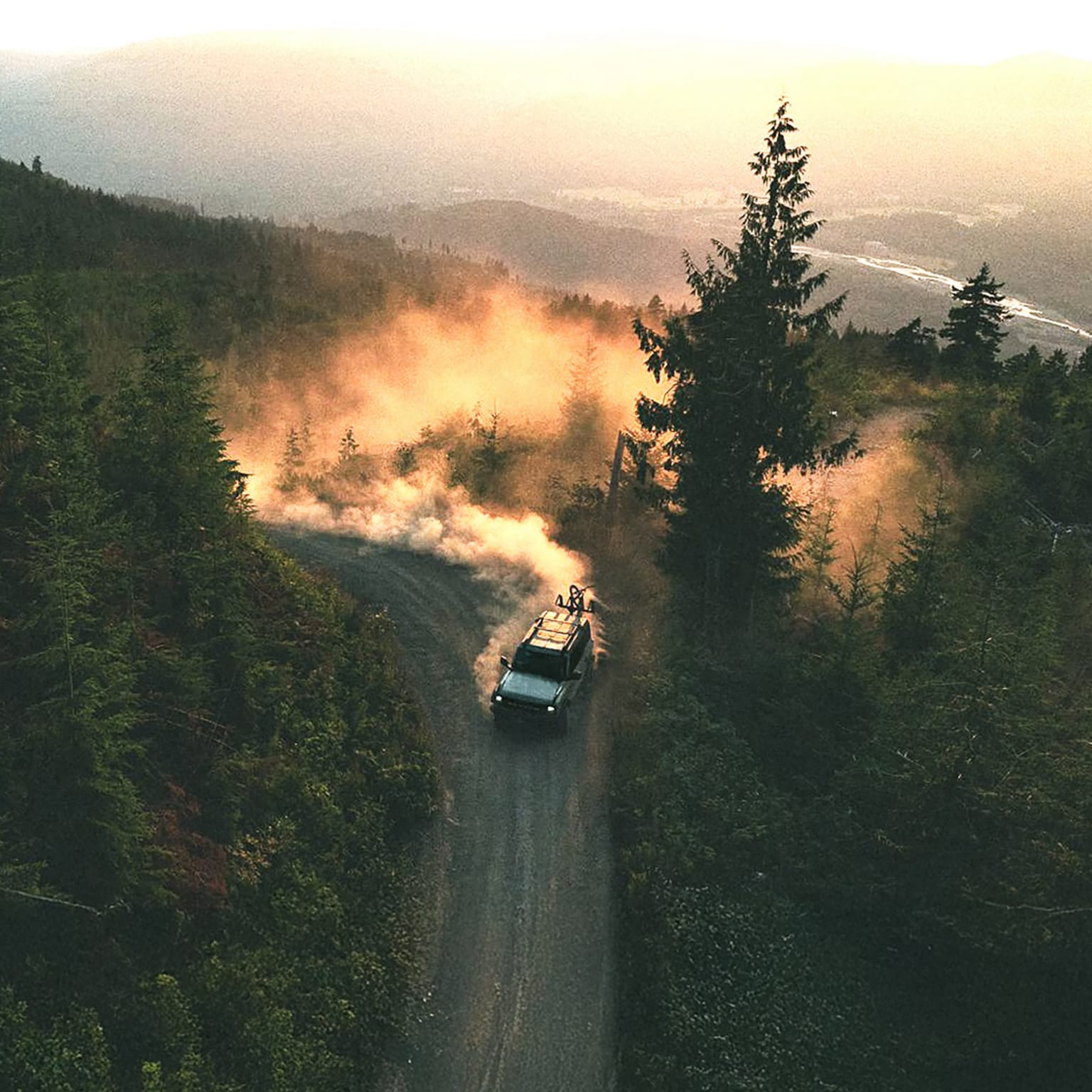 An off-road vehicle driving on a mountain road surrounded by evergreen forests, kicking up dust.