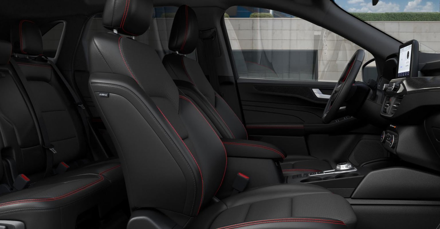 Interior of a vehicle with black leather seats and red accents, with a building or structure in the background.