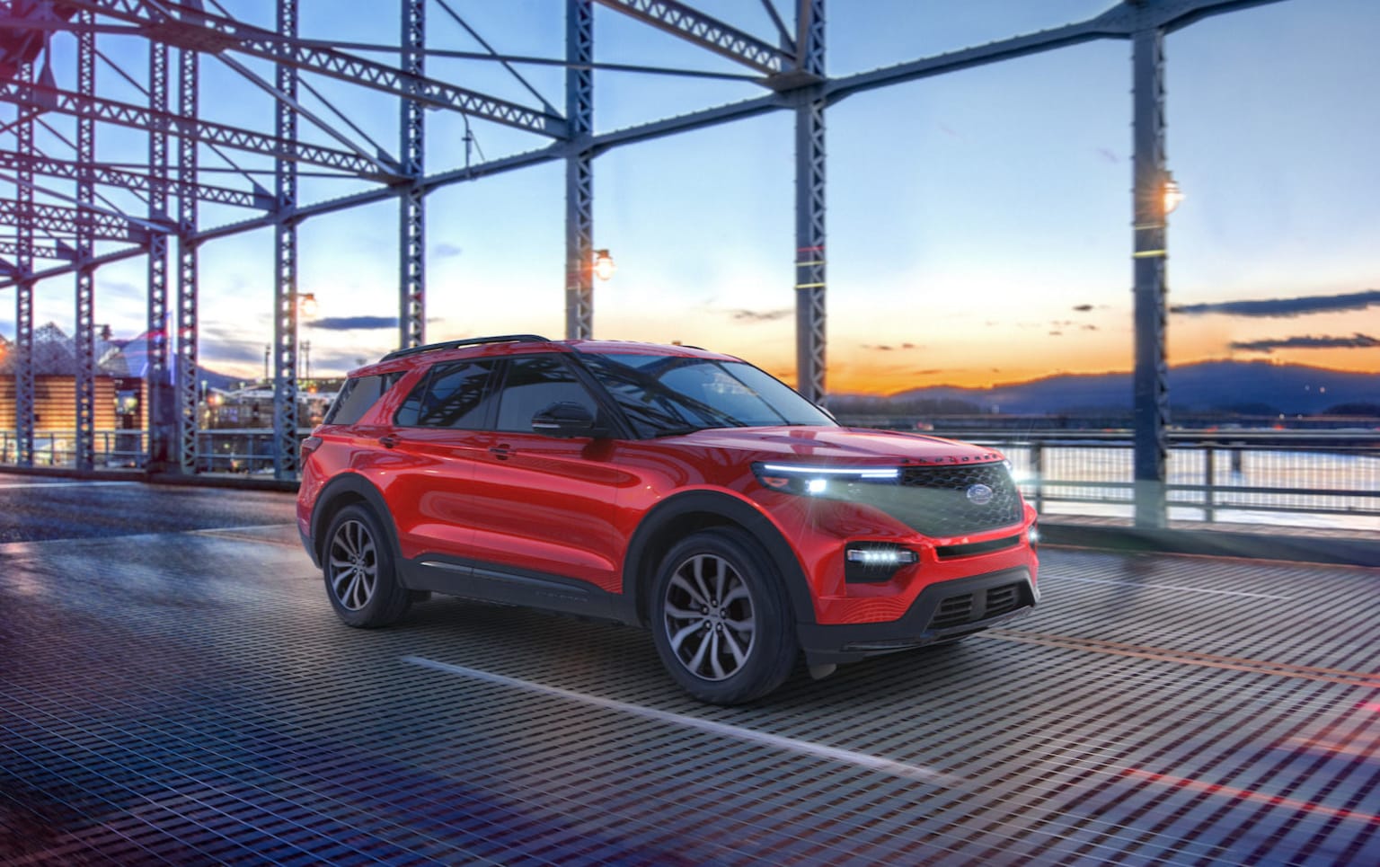 a red suv is parked in a parking lot near a large metal structure with a sunset in the background