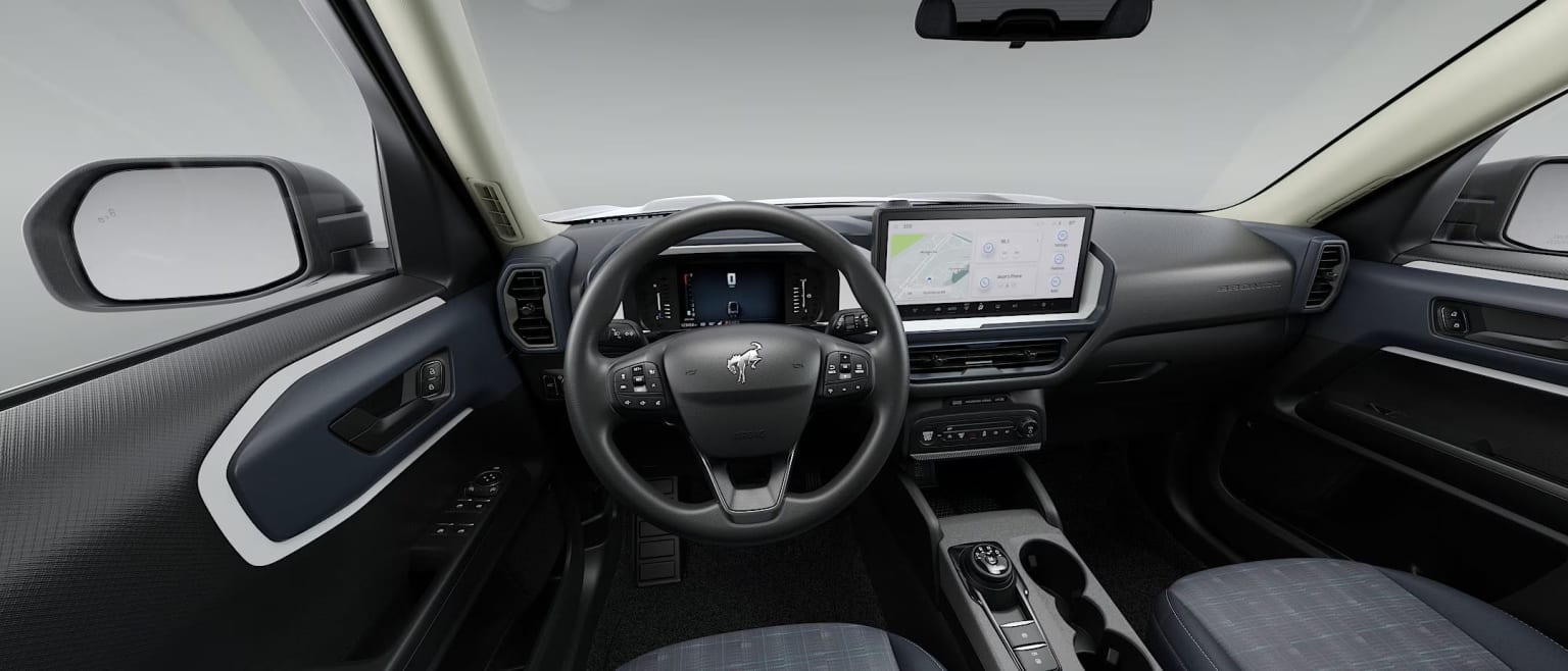 Interior view of a car with a steering wheel and dashboard against a plain white wall
