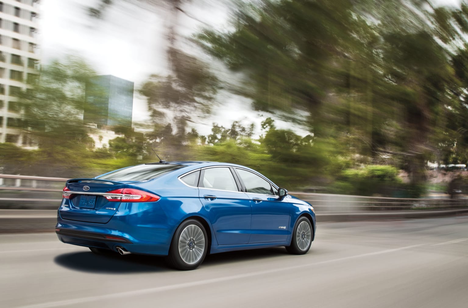 a blue car driving down a street next to a tall building with lots of trees in front of it