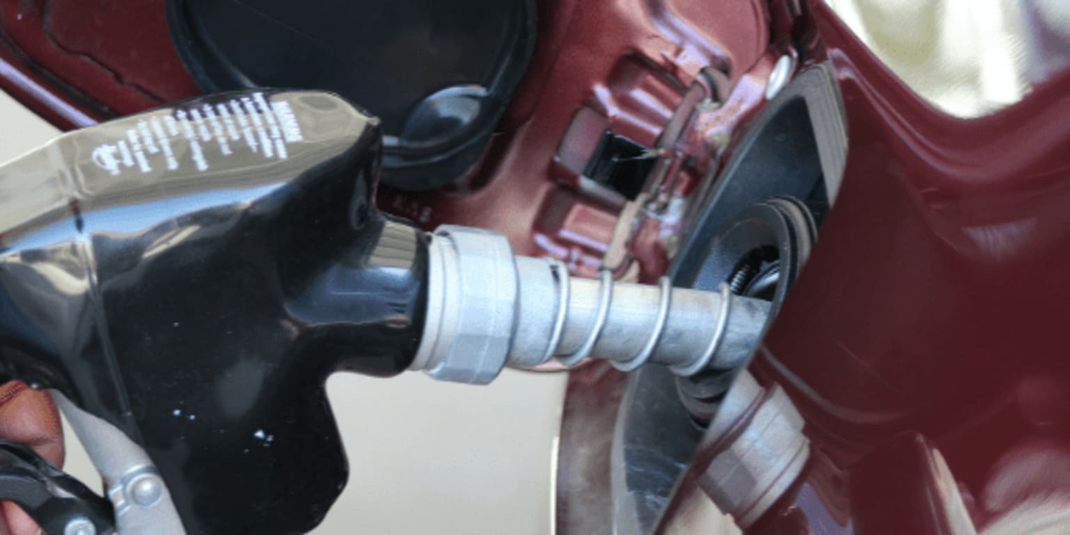 a close up of a gas pump with a person holding a wrench and a car in the background