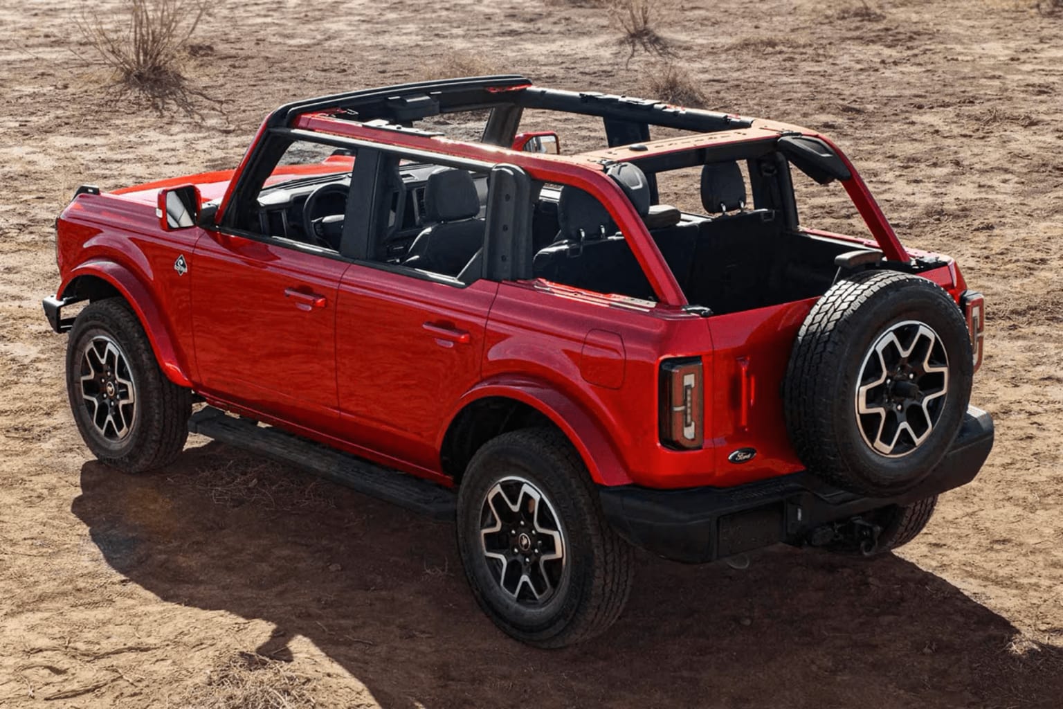 A red off-road vehicle with a rugged, open-air design on a dry, sandy terrain surrounded by sparse vegetation.