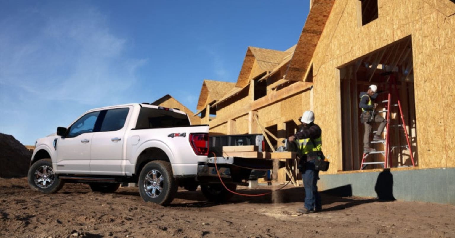 a white truck parked in front of a house under construction with two men working on the back of the truck