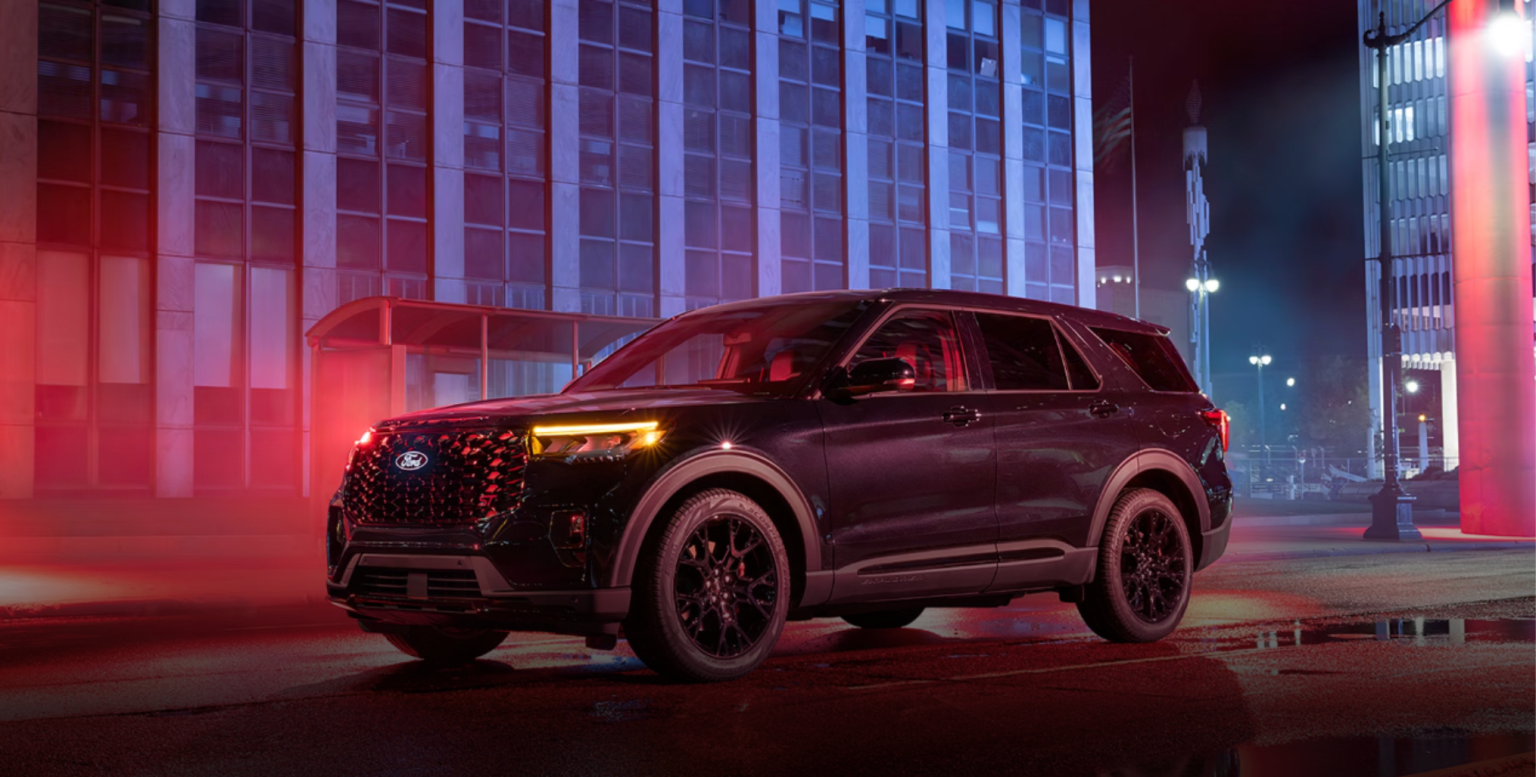 A dark SUV parked on a wet city street in front of a modern office building illuminated by red and blue lights.