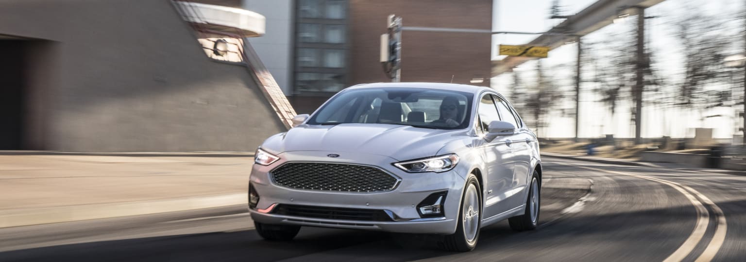 a silver car driving down a street next to a tall brick building with a clock on it's side